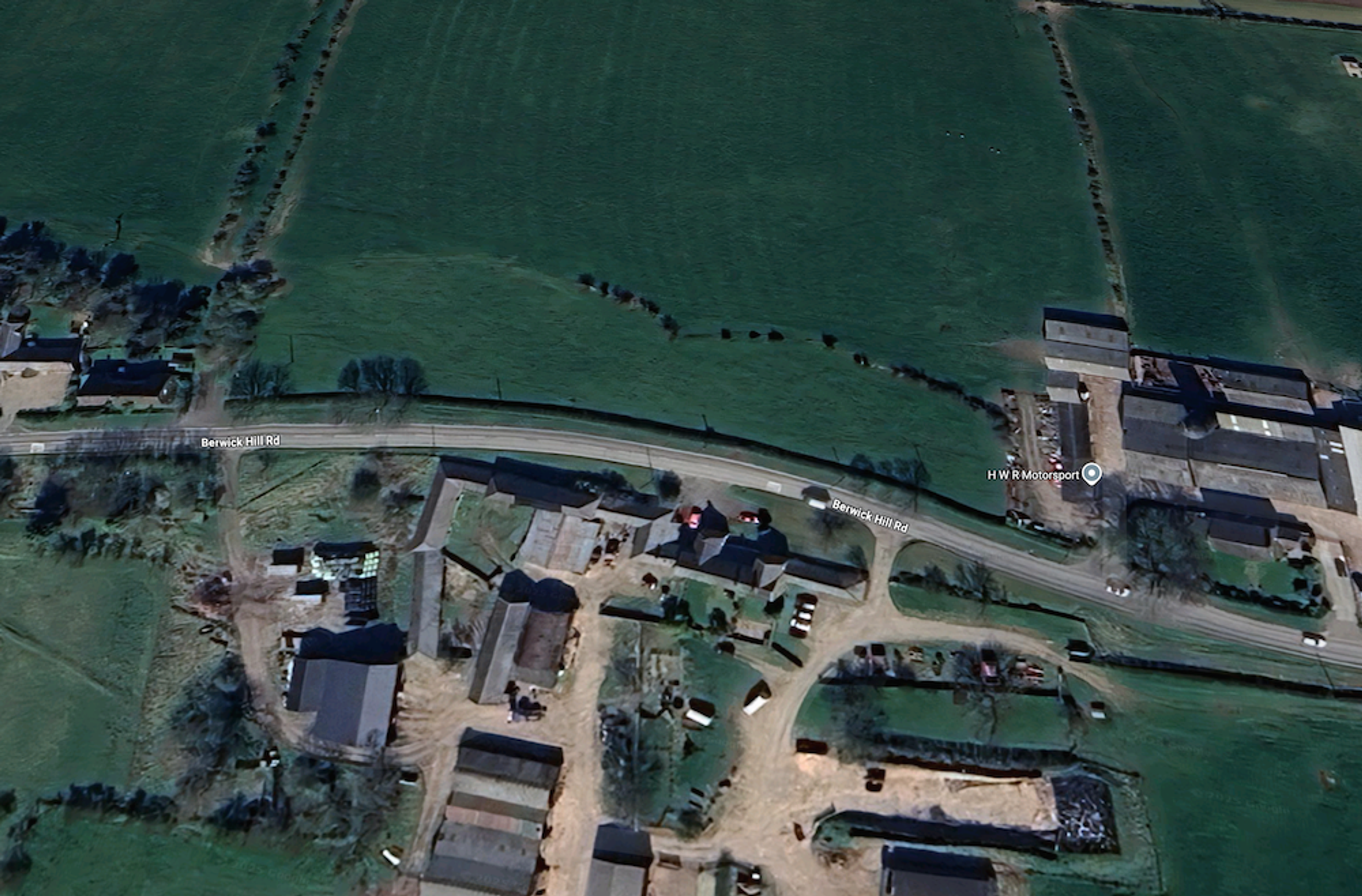 Aerial view of a roadside farmstead with sheds and yards, hedged fields stretching away on either side