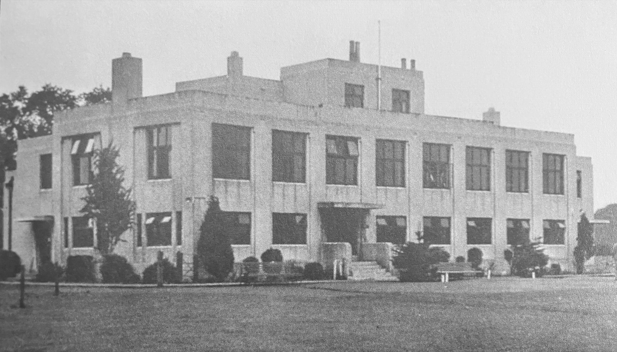 Black and white photograph of a flat-roofed Art Deco clubhouse with long window bands, seen across the lawn