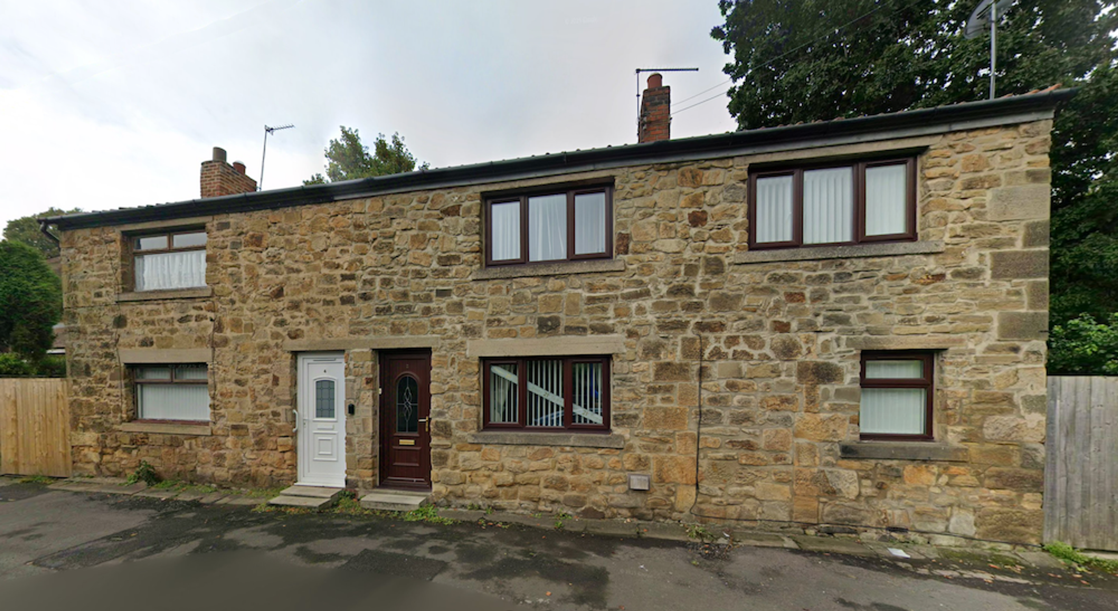 A long low stone cottage terrace with modern windows and two front doors, standing directly on the street