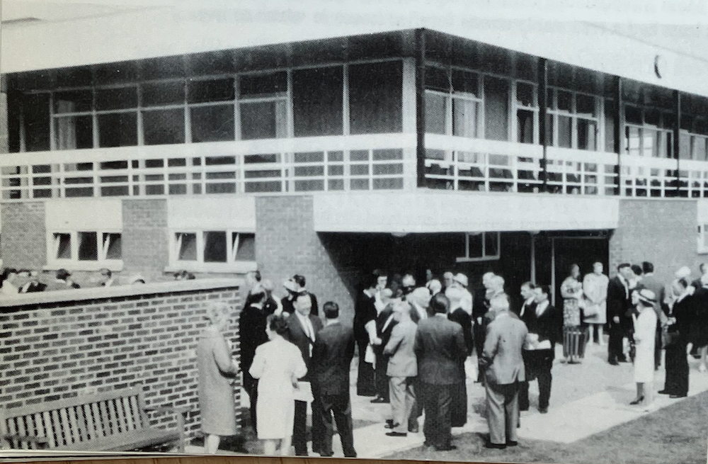 Black and white photograph of a crowd of people in coats and hats gathered outside a modern flat-roofed sports centre at its opening