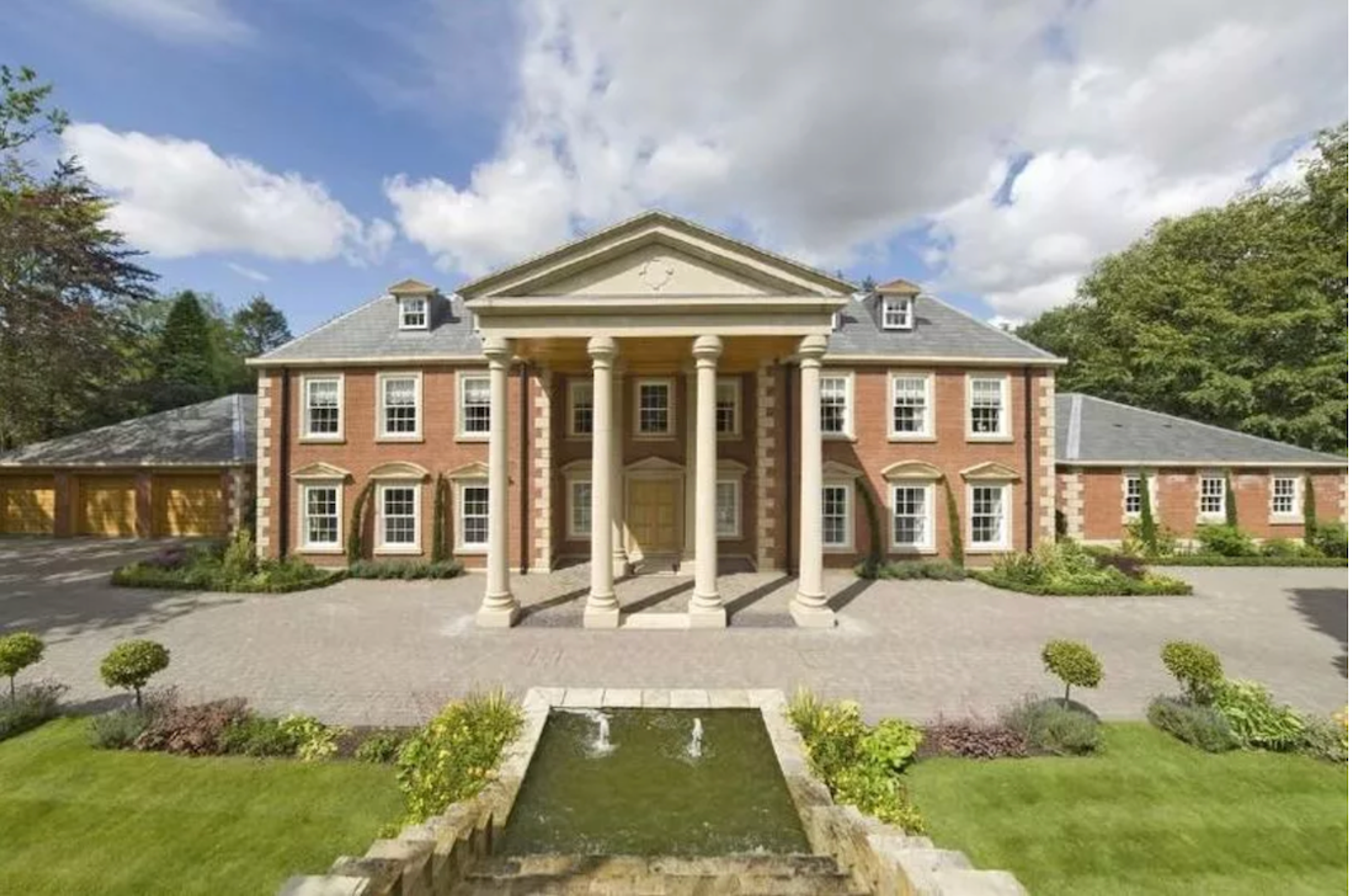 A large modern neo-Georgian mansion with a pillared portico and pedimented centre, a formal water feature on the lawn in front