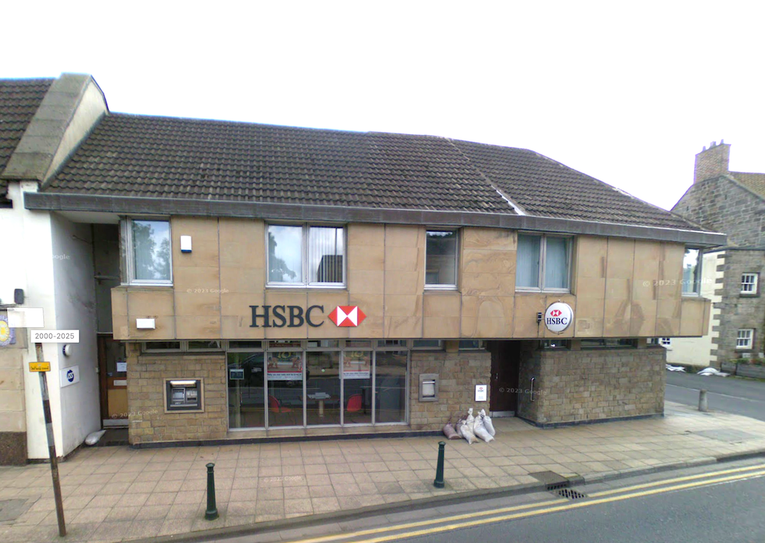 A single-storey stone-clad bank branch with an HSBC sign and a pantiled roof, bollards along the pavement in front