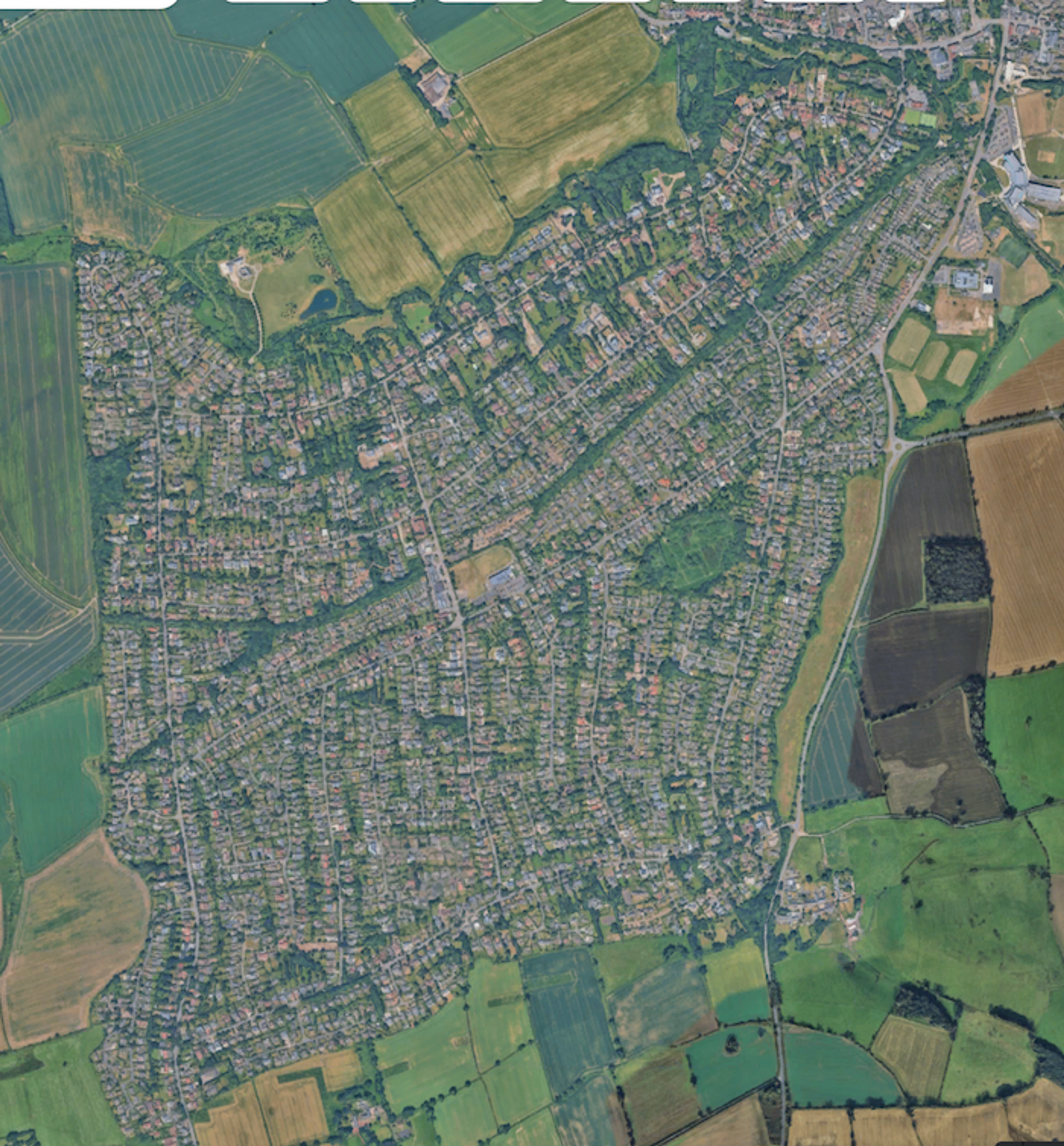 Aerial view of a large tree-lined housing estate laid out on a grid, surrounded on all sides by open farmland
