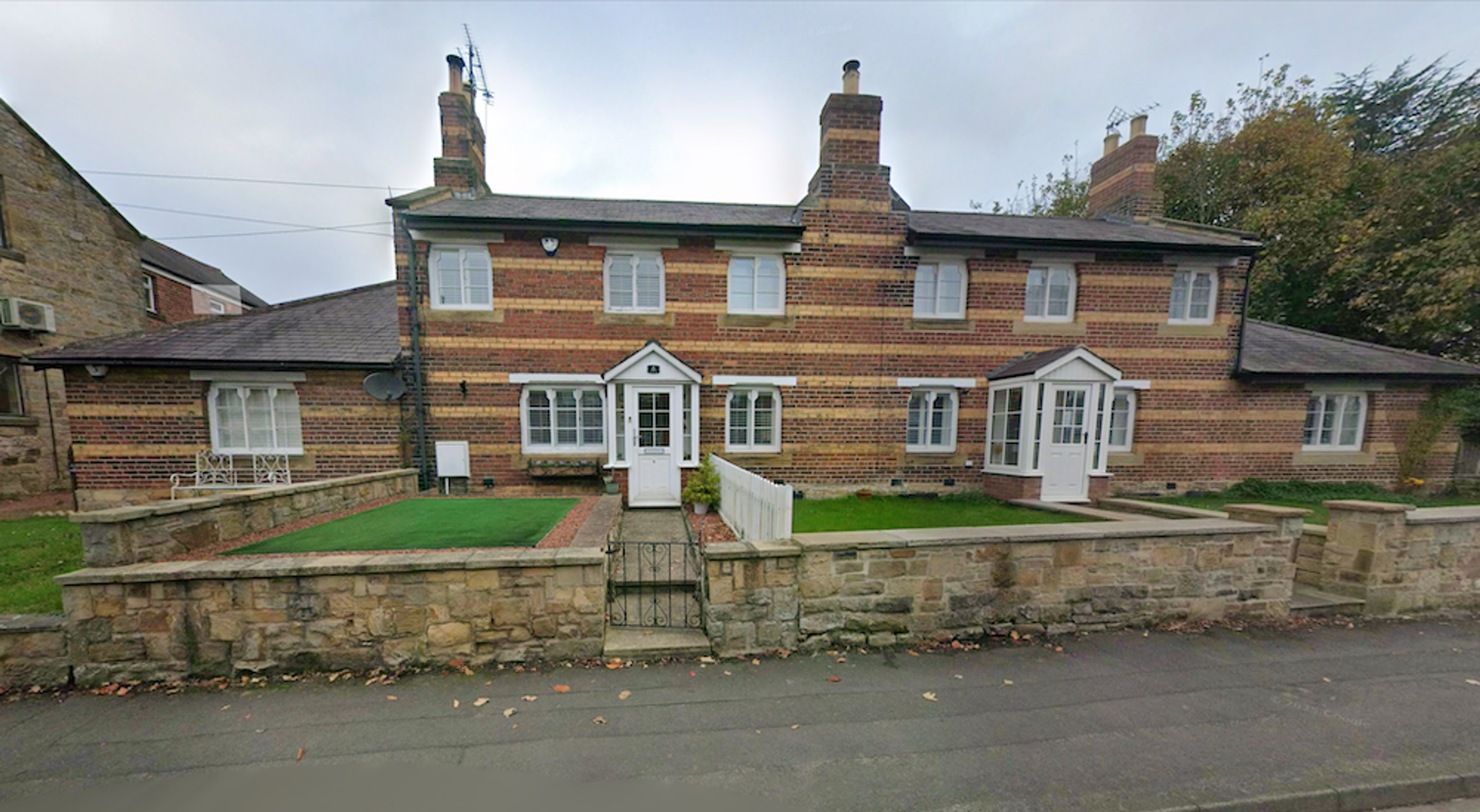 A terrace of cottages in patterned brick with white porches and sash windows, set behind a low stone wall