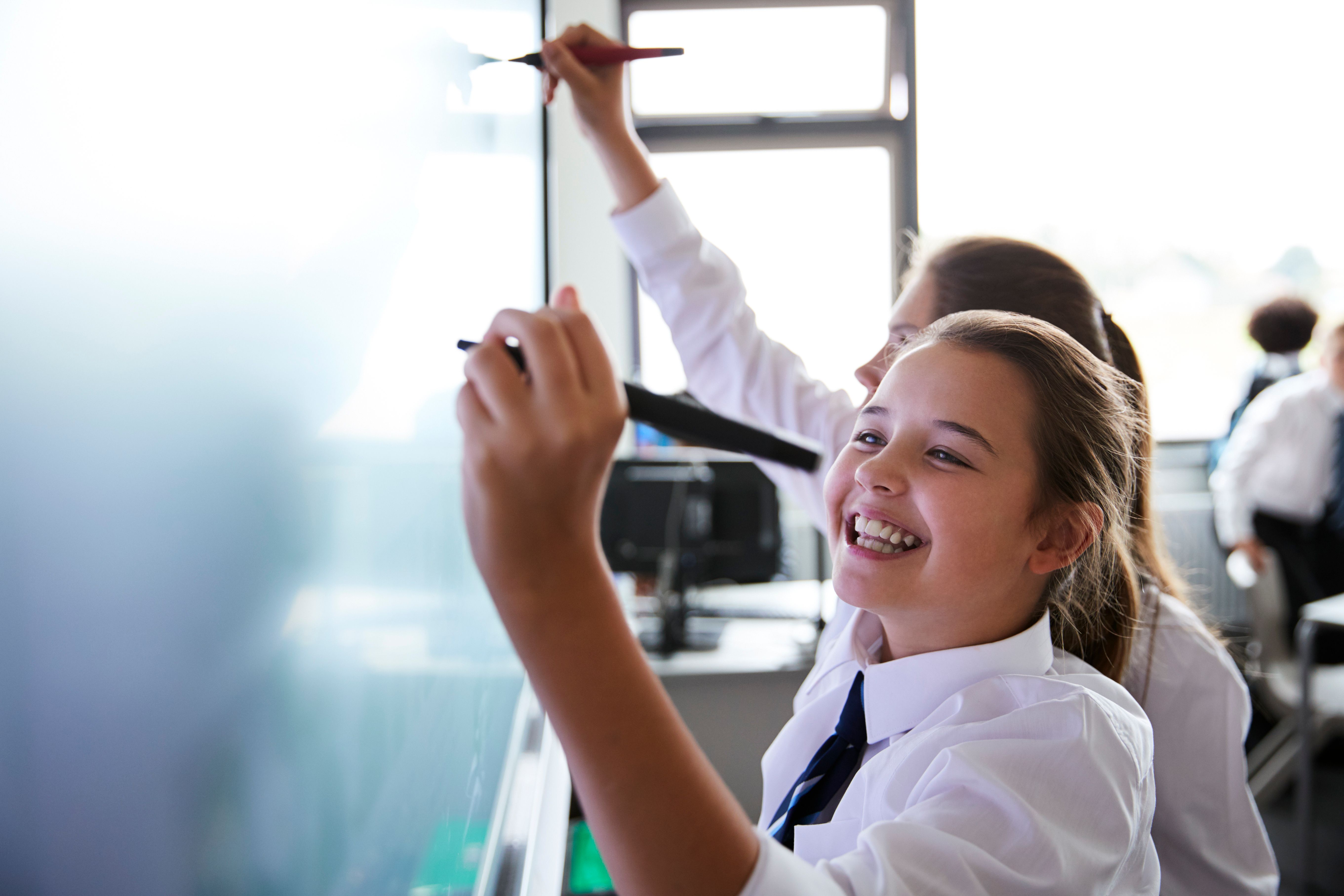 A smiling student in school uniform writing on an interactive whiteboard