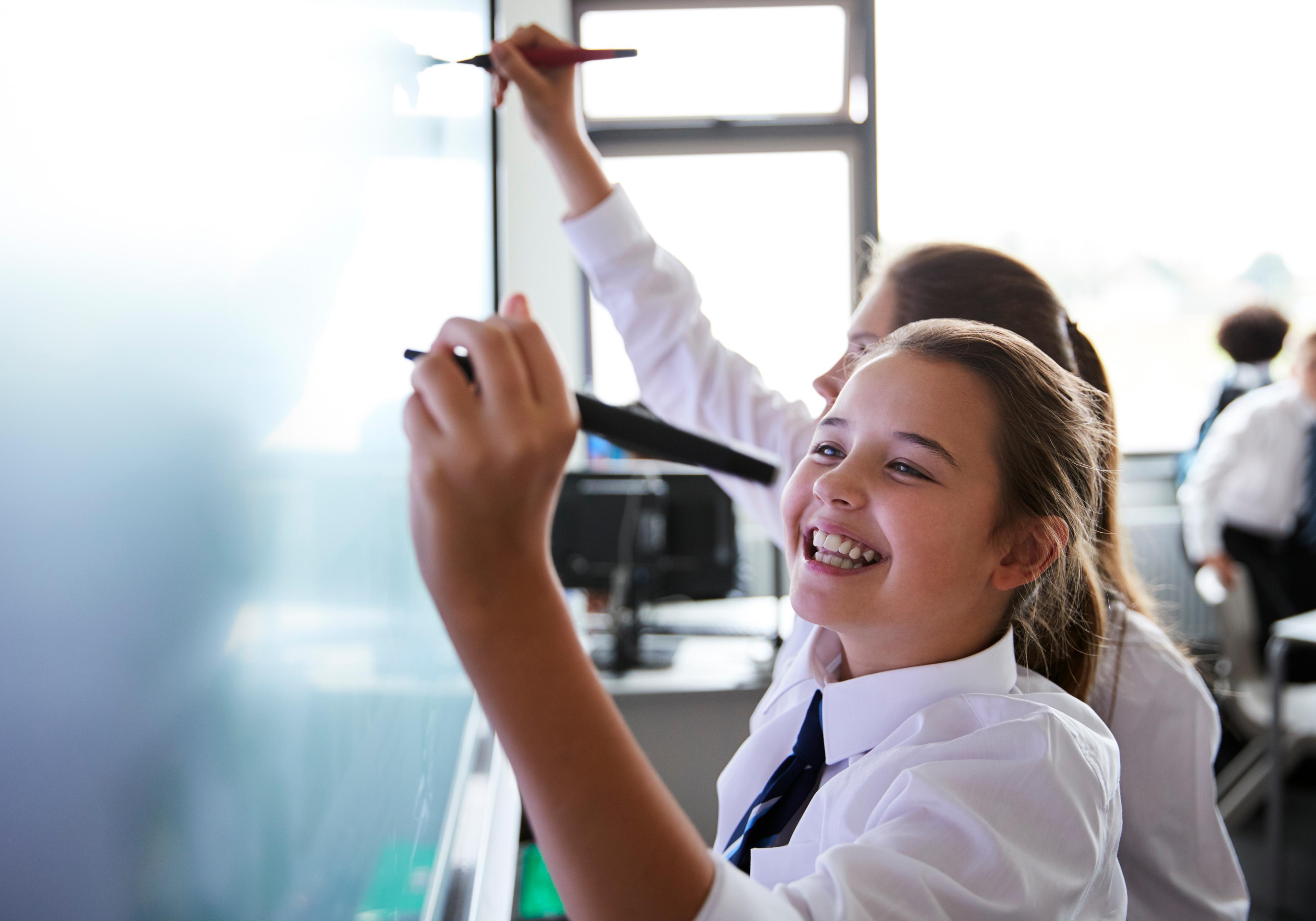 A smiling student in school uniform writing on an interactive whiteboard
