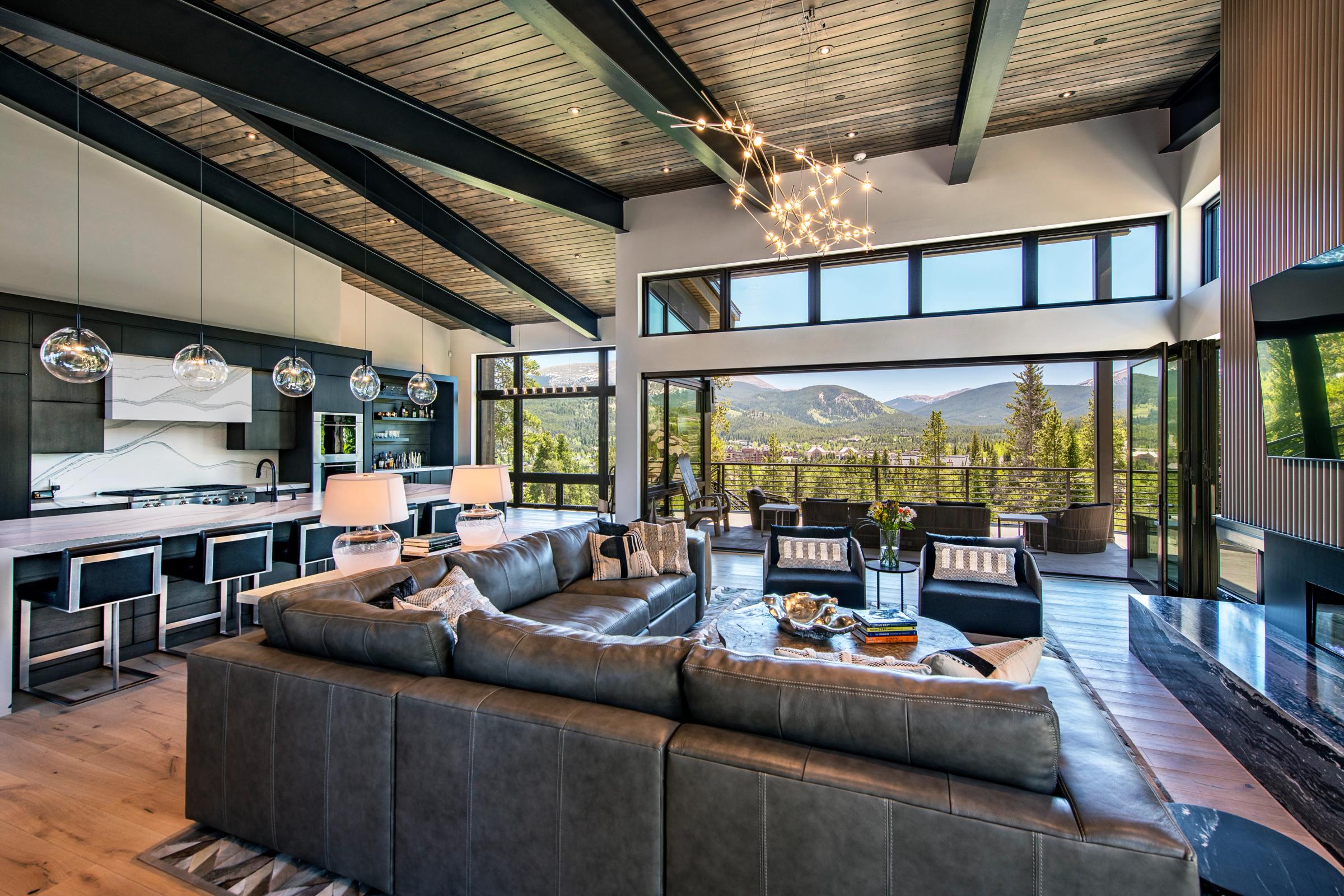Open great room with a leather sectional and open kitchen, its operable glass wall drawn back to a deck overlooking Breckenridge and the surrounding peaks