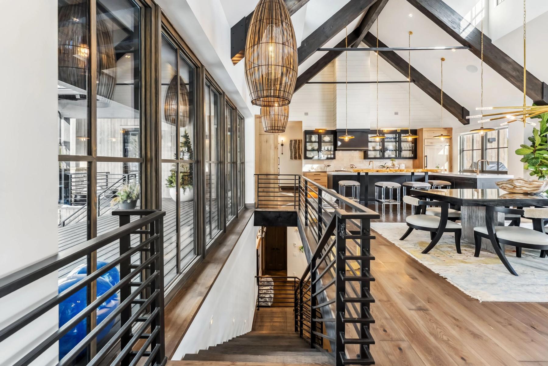 Great room of the Barton residence under exposed timber trusses, with blackened steel railings and the dining area beyond