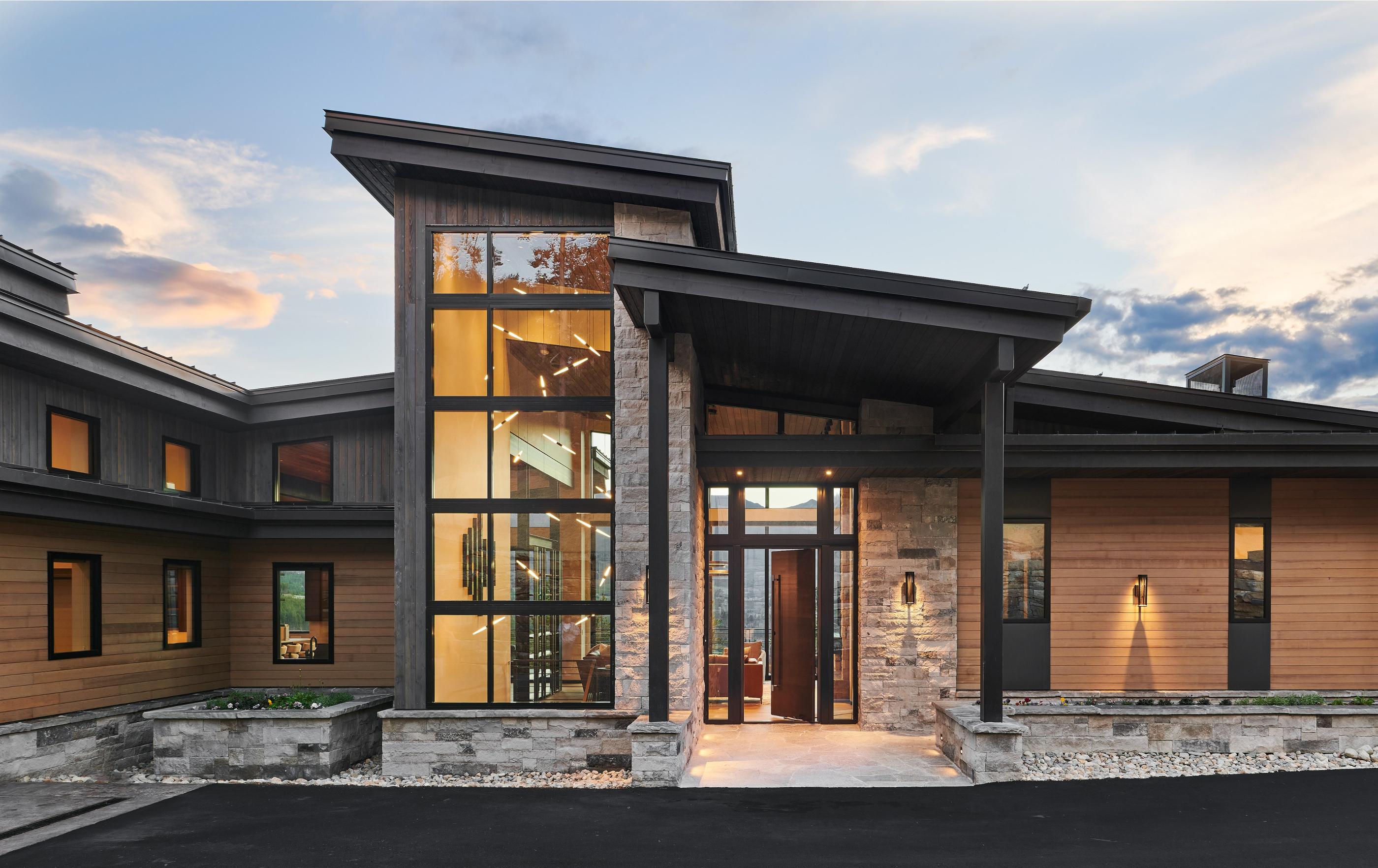 A completed Iron Forest custom home at dusk, timber and stone with the windows lit