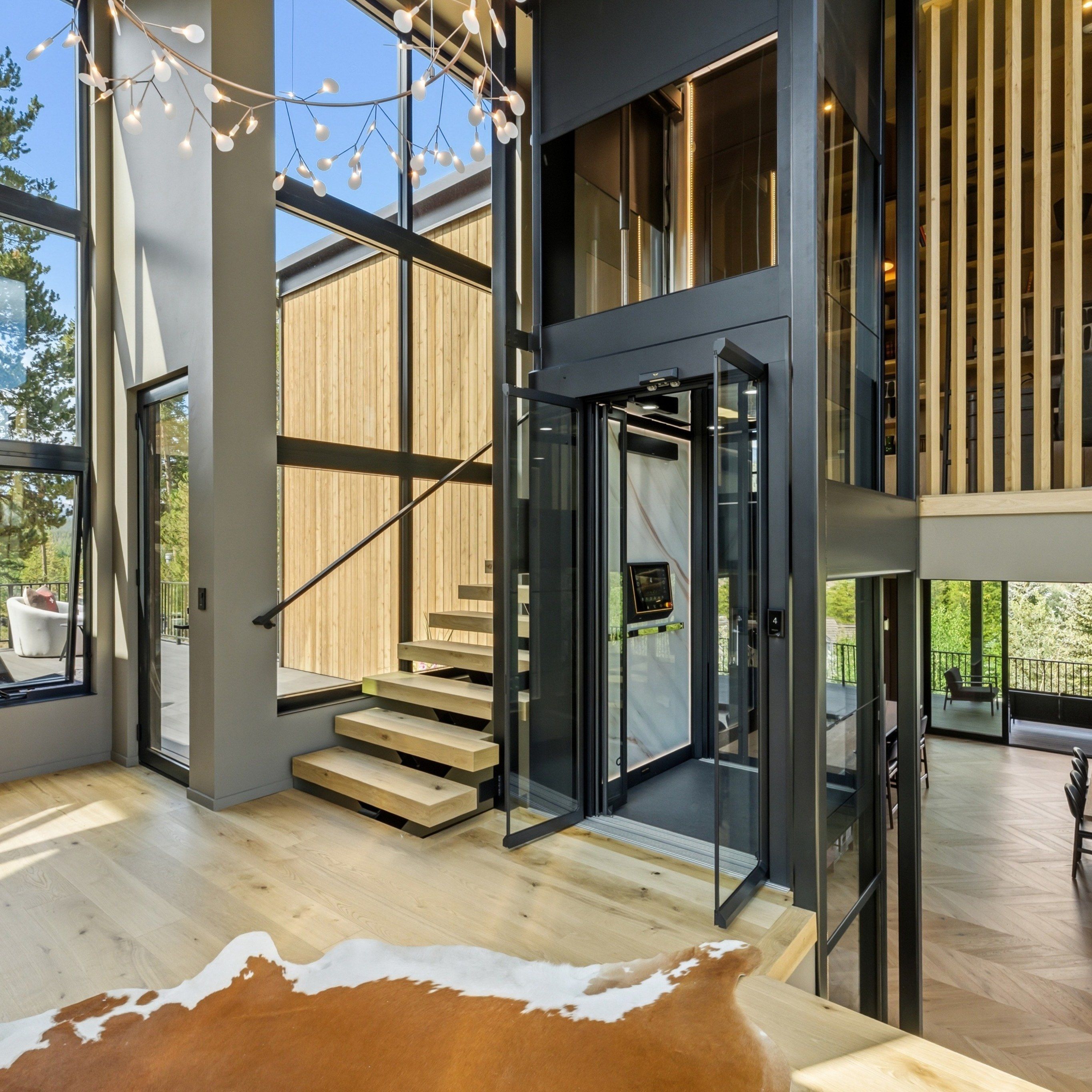 Double-height entry with a glass-and-steel elevator, floating oak stair treads, a branching pendant light and a cowhide rug