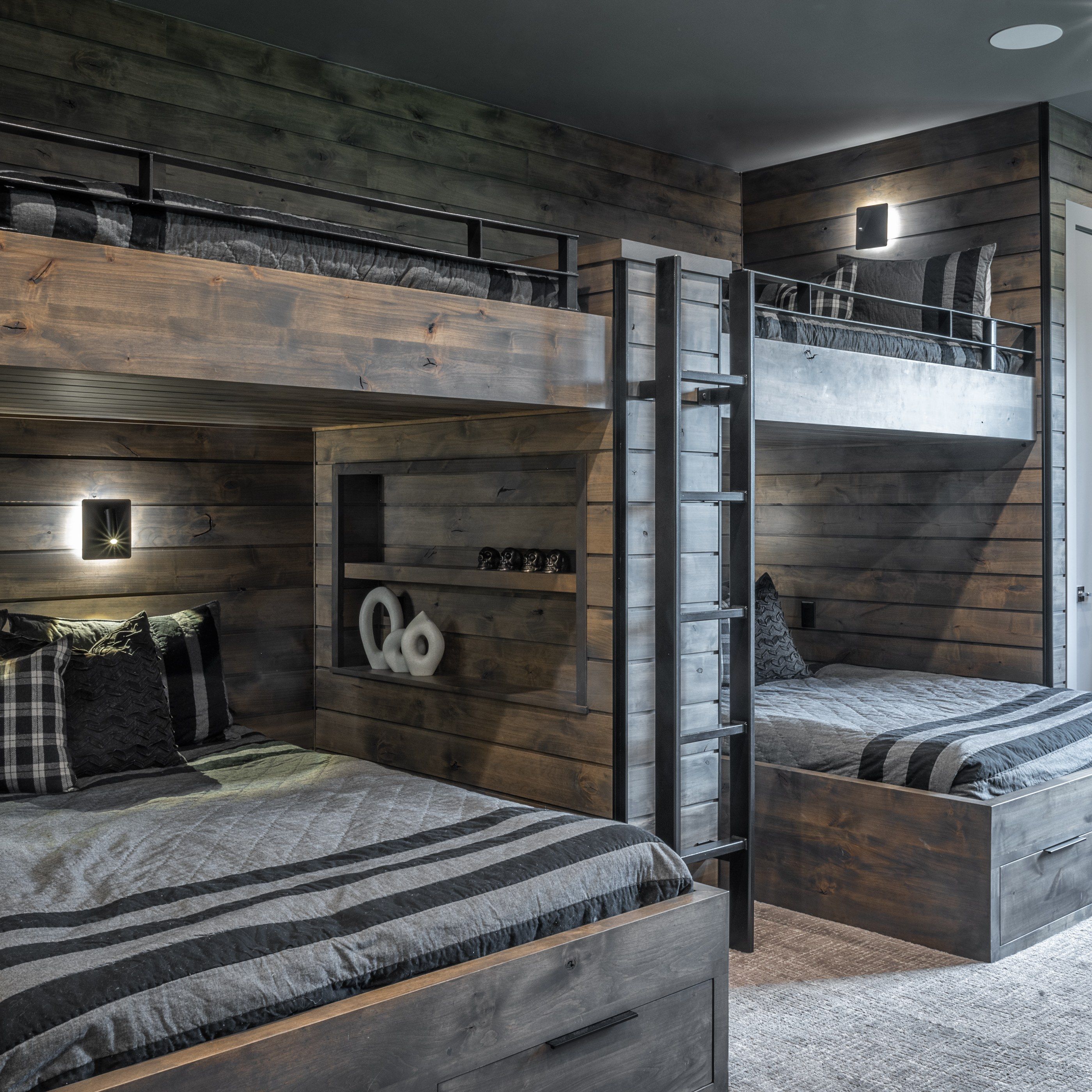Bunk room with built-in queen-over-queen bunks in grey-stained wood, a black steel ladder and reading lights