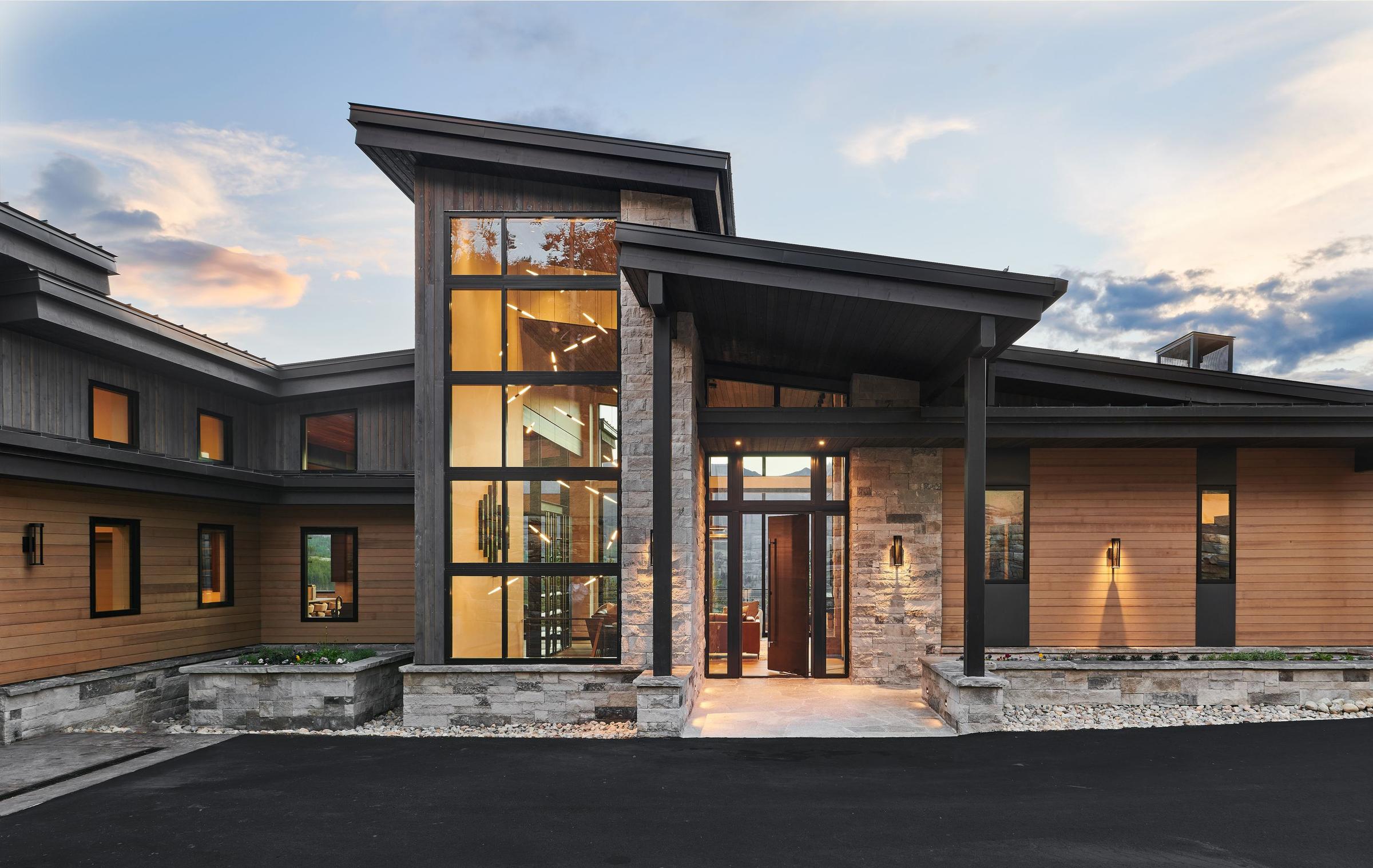 The Summit Estates residence at dusk, stone and timber with its windows lit and the valley beyond
