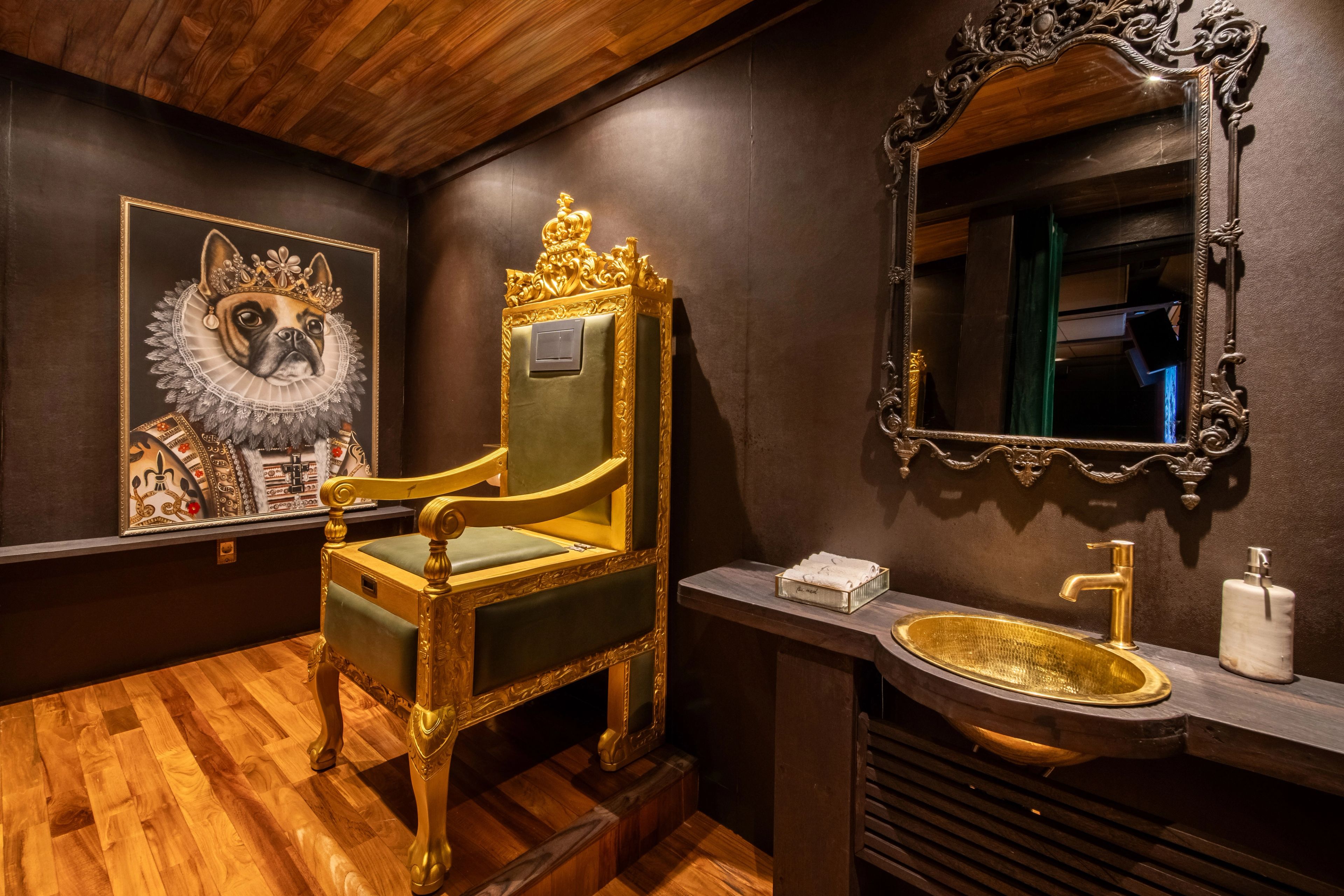 A gilded throne chair beside a brass basin and an ornate mirror in the basement powder room.