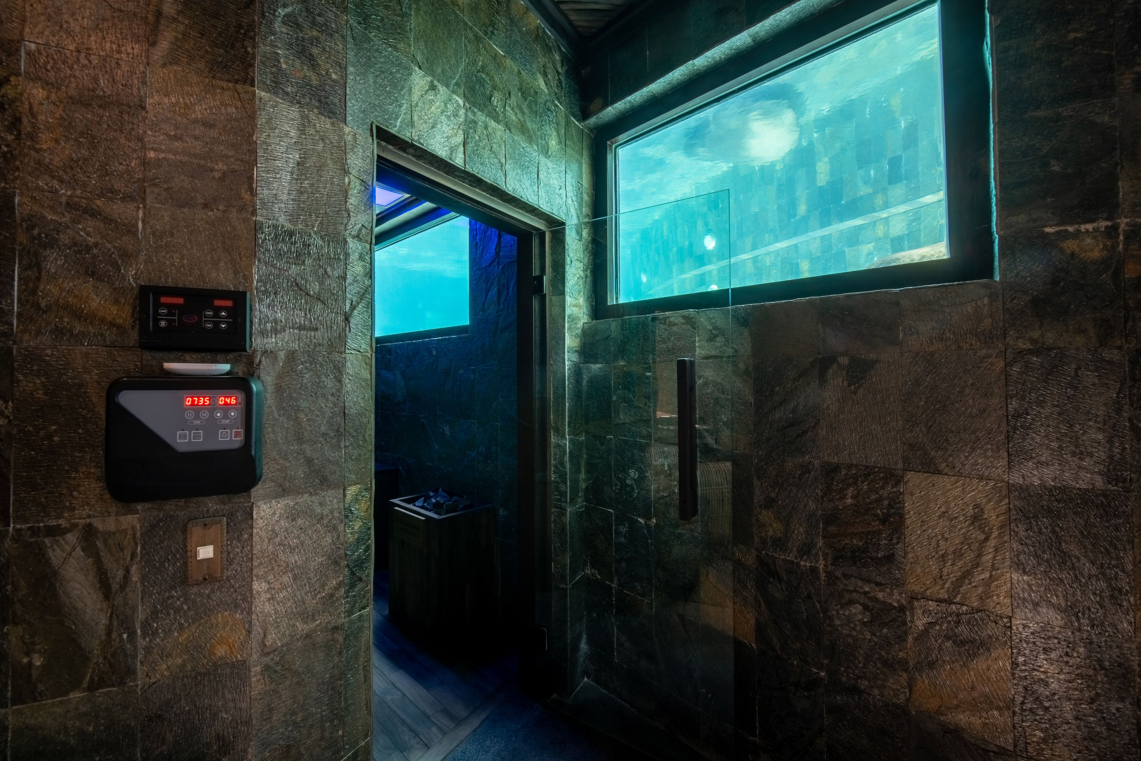 A stone-tiled corridor in the spa lit by a glowing aquarium window set into the wall.