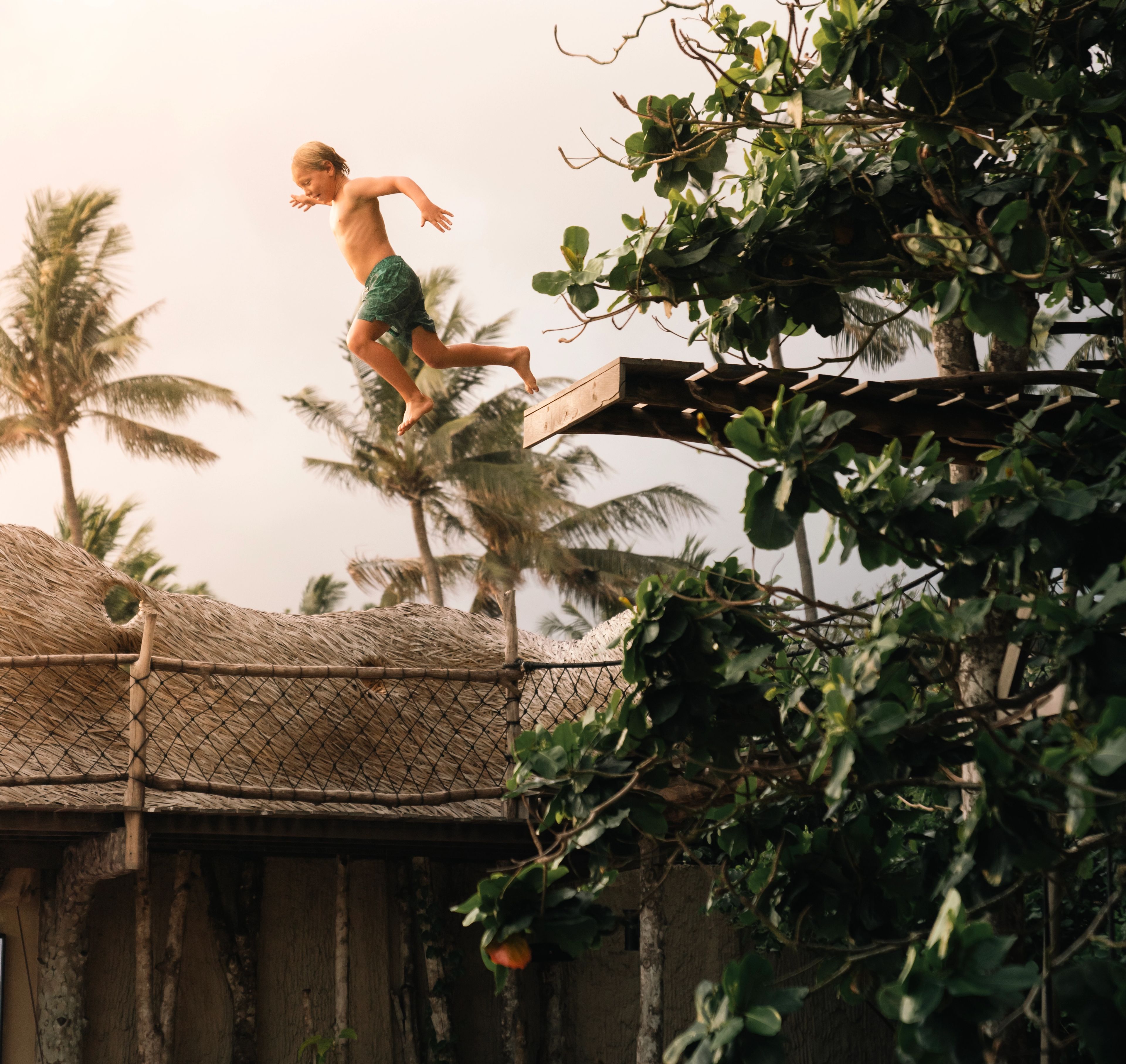 Child jumping off a wooden platform near the treehouse rooftop