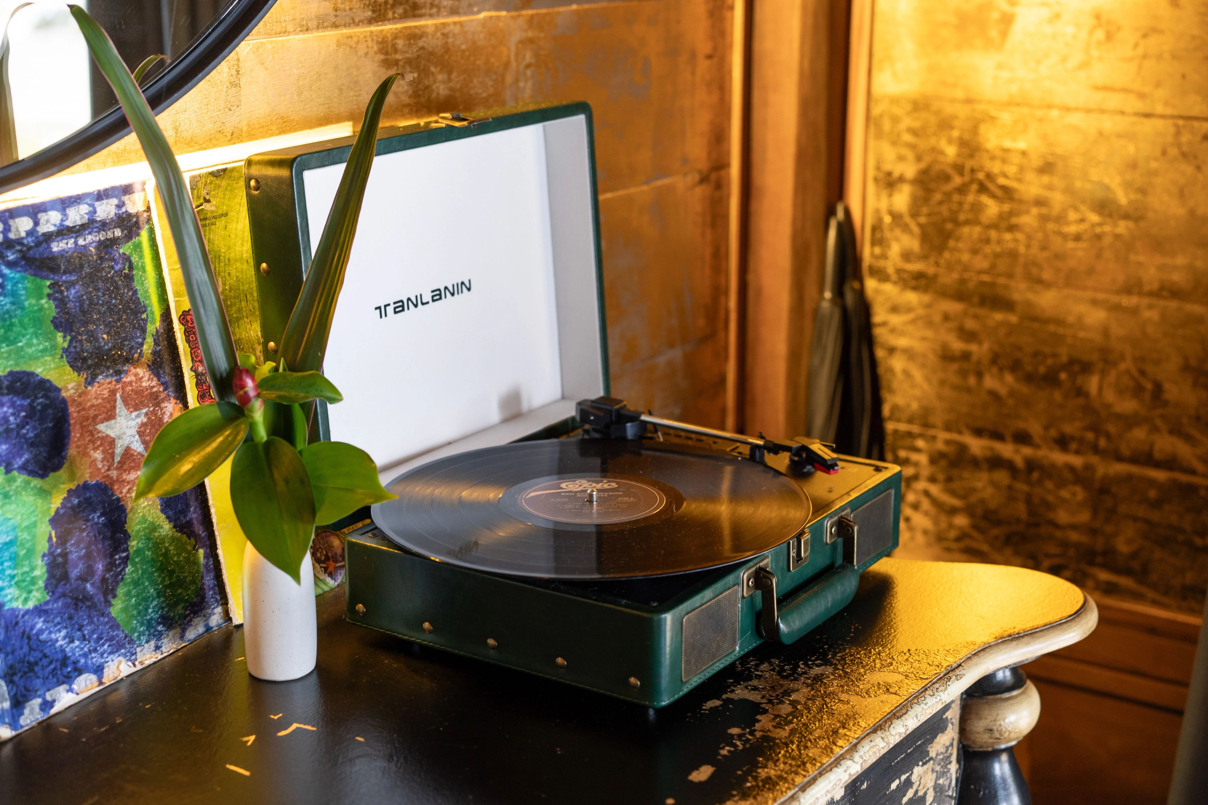 A turntable with a record on the platter, beside a vase and framed artwork.