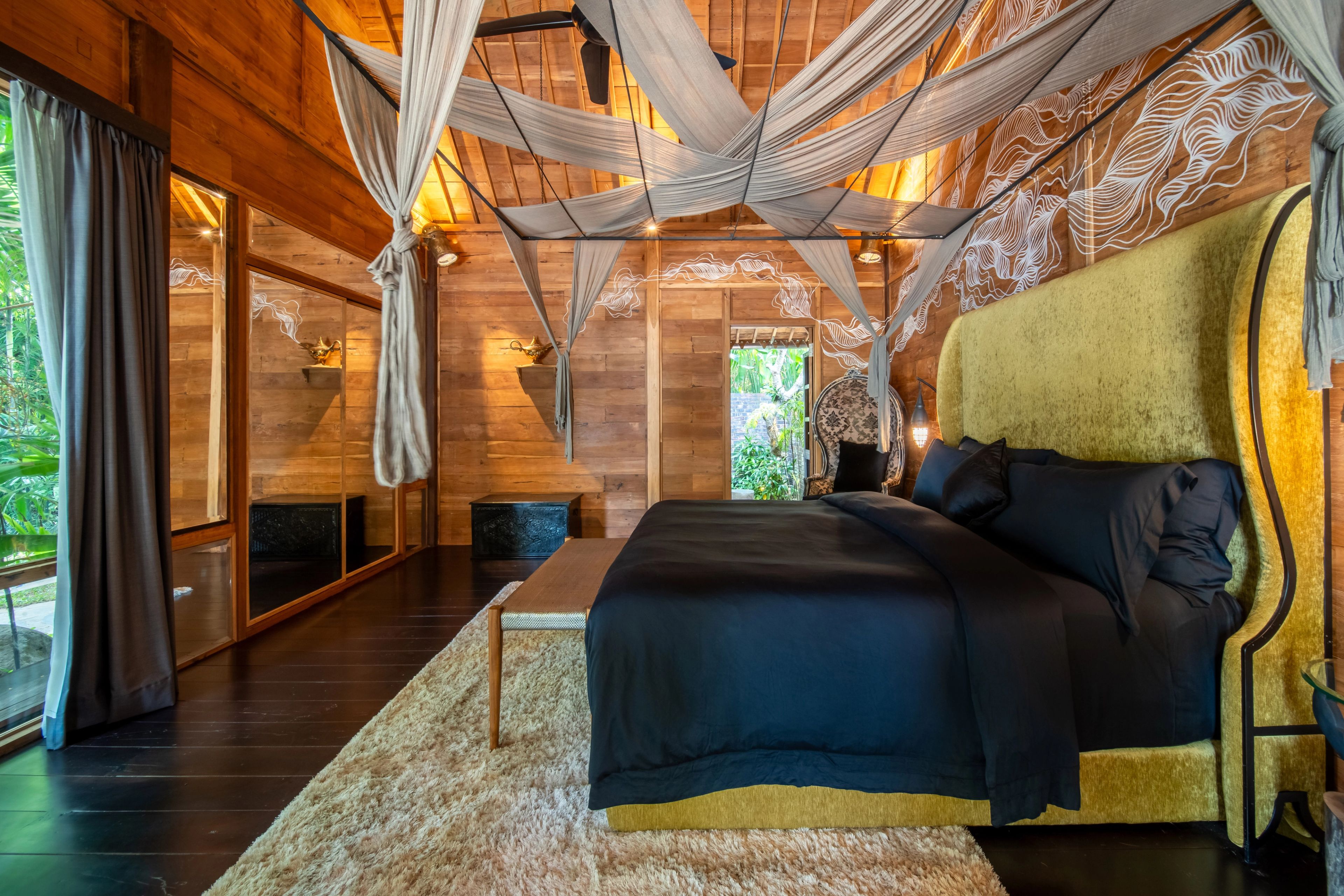 A bed in dark linen against a tall olive headboard, mosquito net gathered above it.