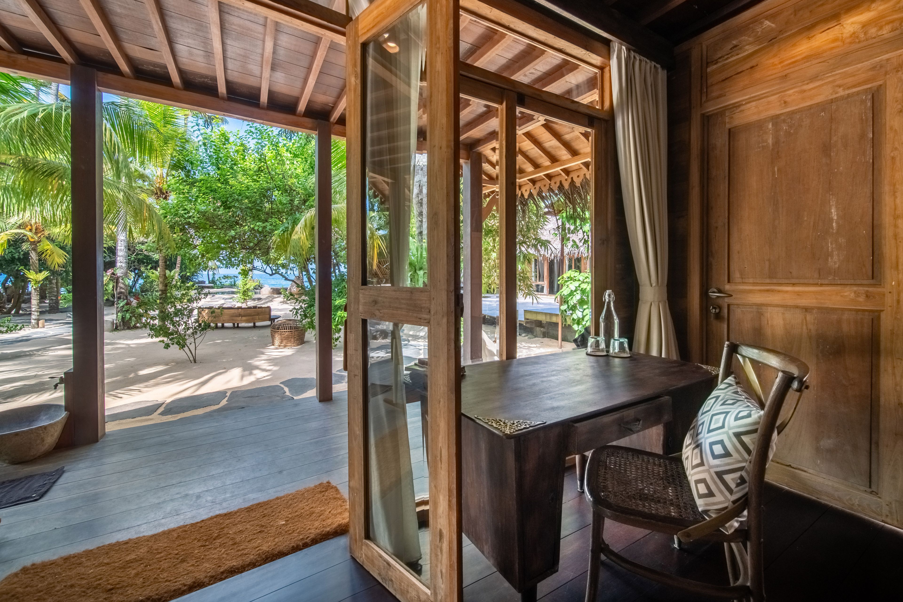 A timber desk and patterned chair beside open doors looking out to the palms and courtyard.