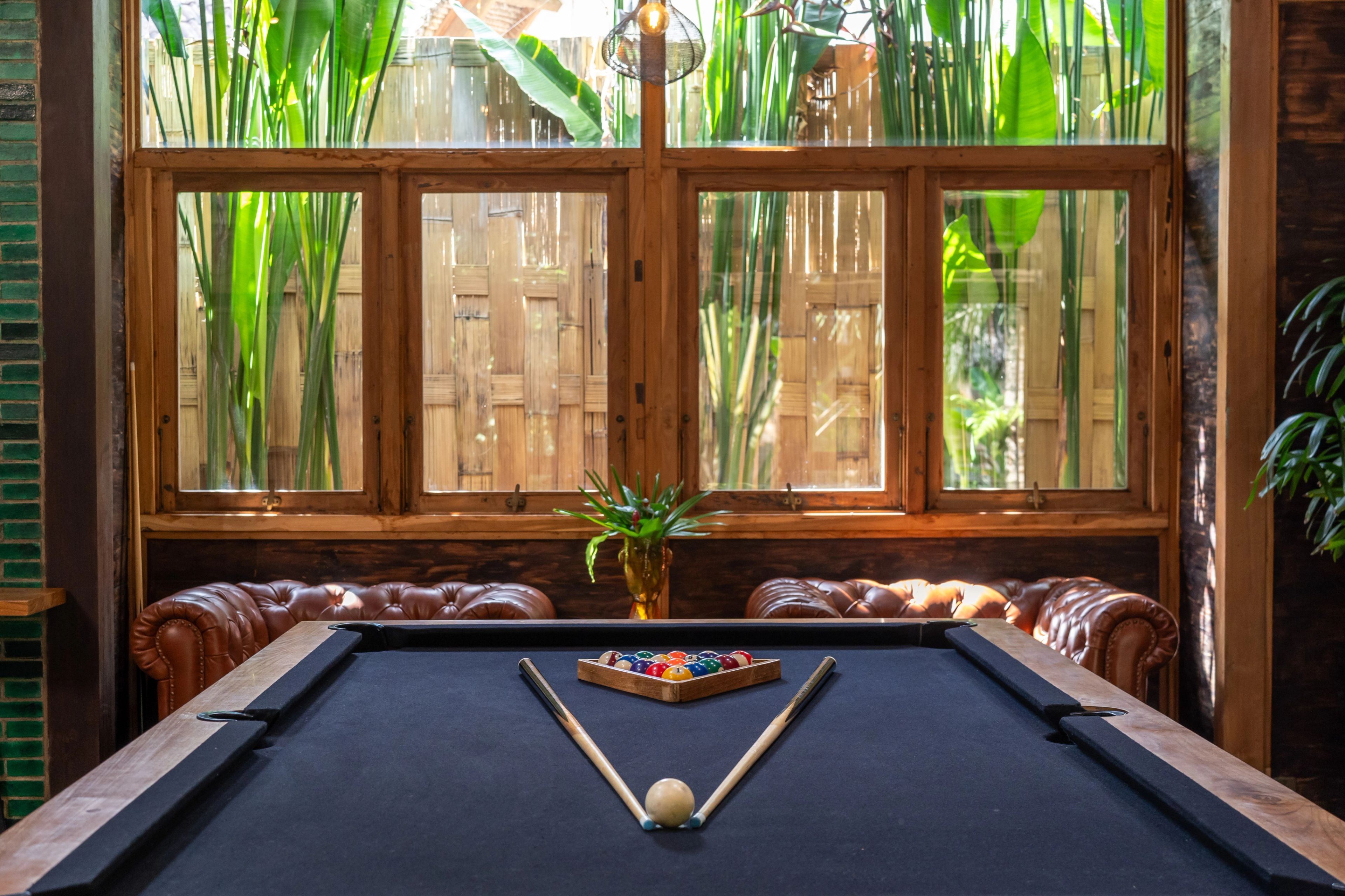 The pool table racked and ready, tan chesterfields either side and bamboo screening the windows behind.