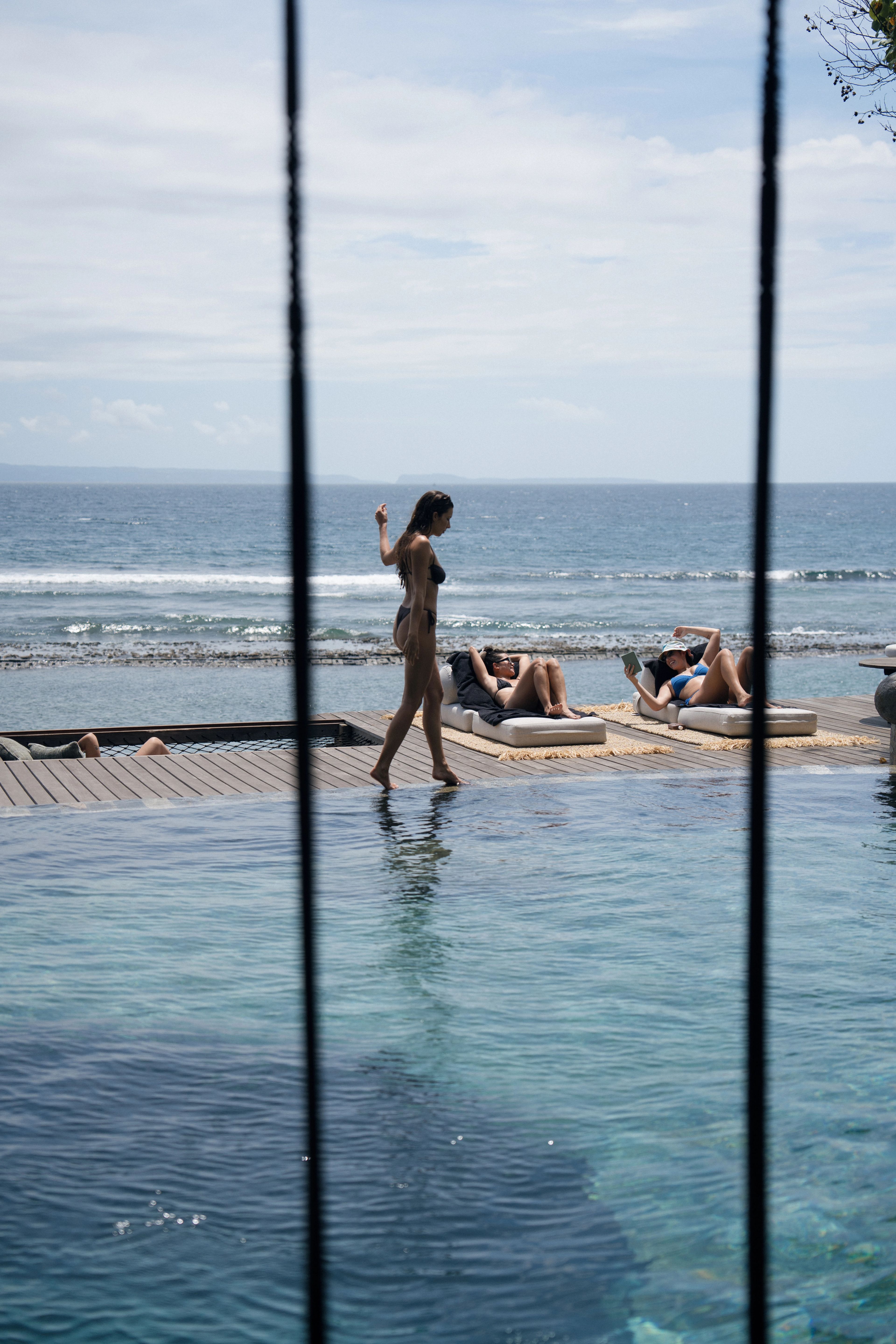 A guest walking the edge of the infinity pool past loungers, the reef and open sea beyond.