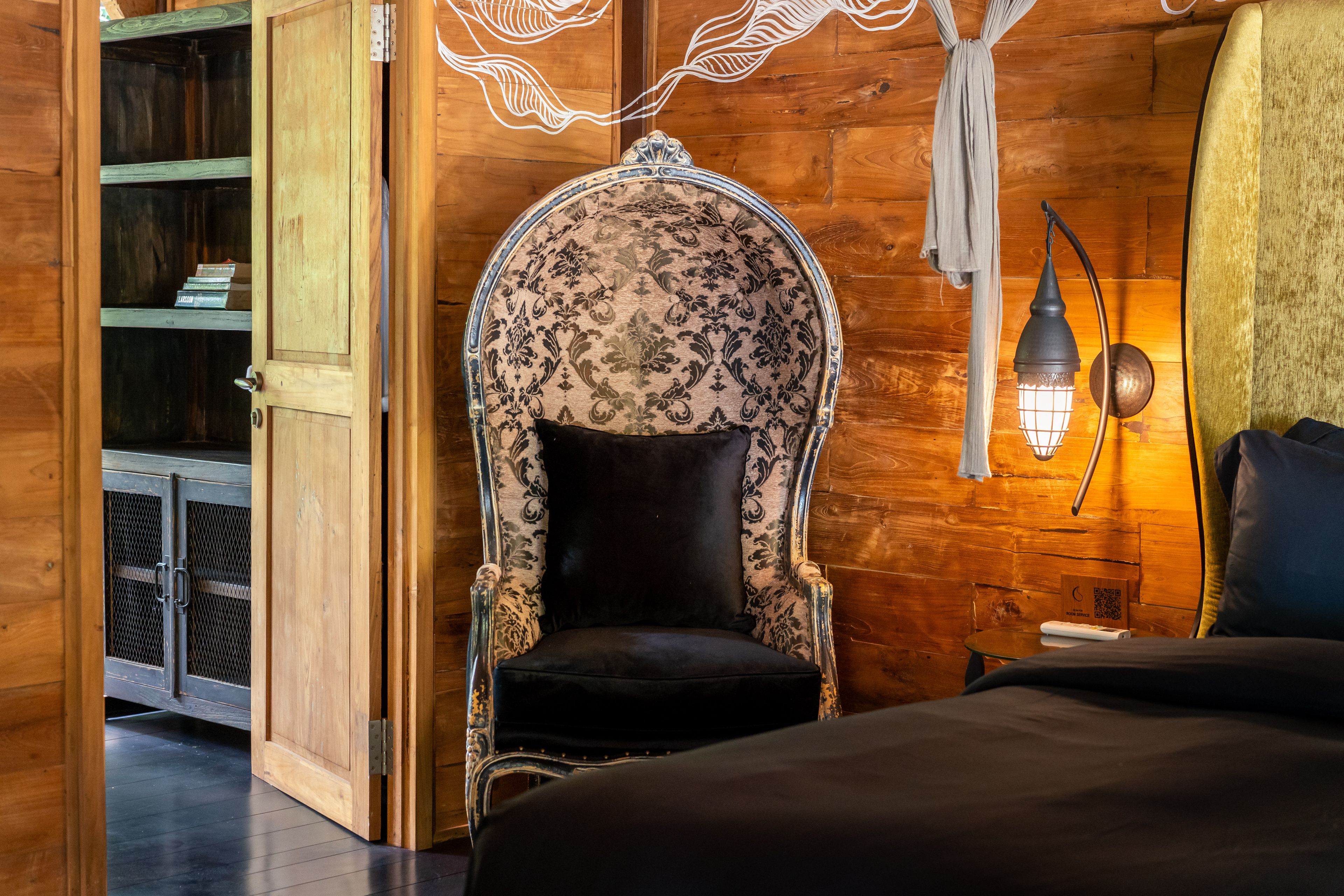 A high hooded armchair in patterned fabric against the timber wall beside the bed.
