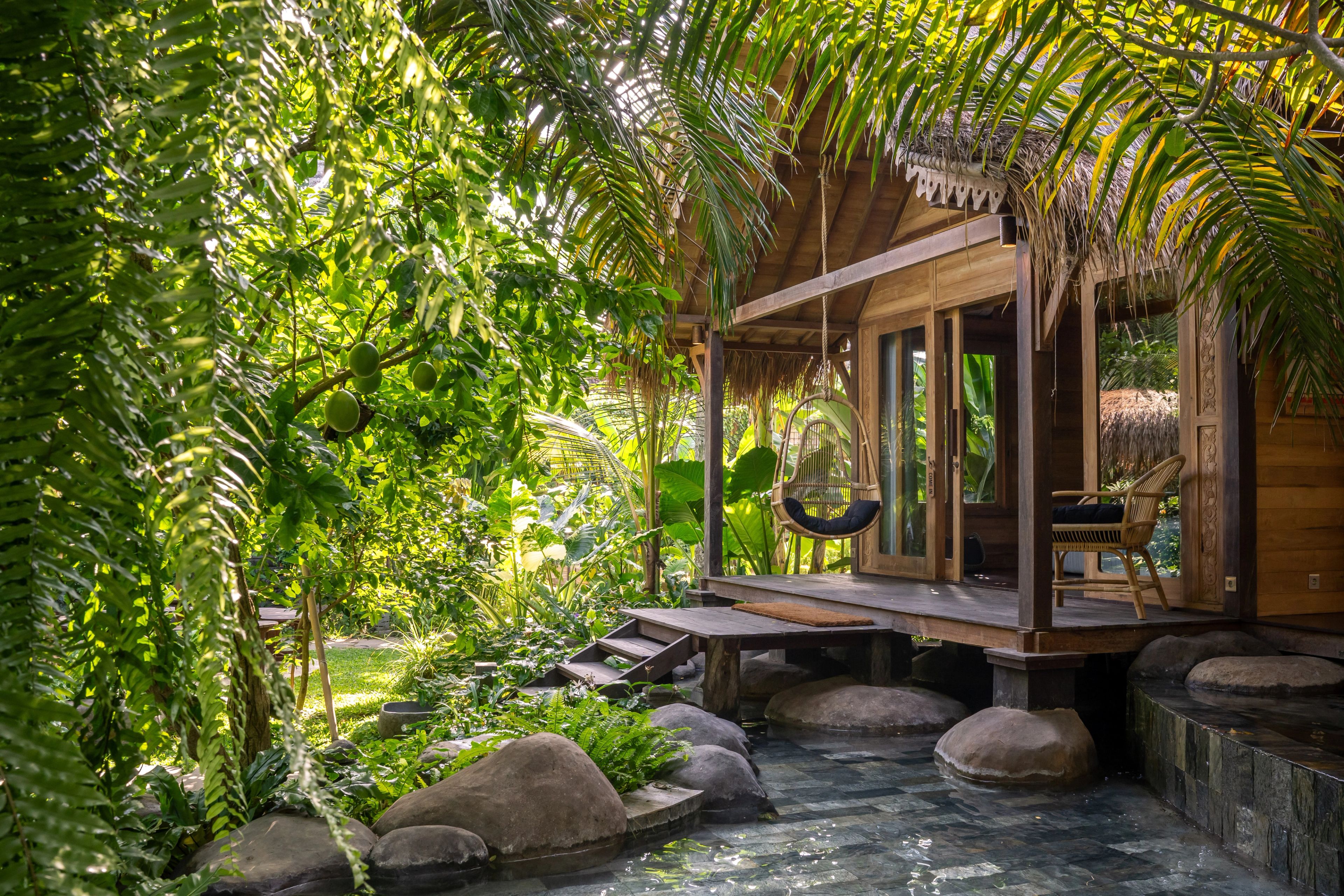 The villa's deck and hanging chair seen through hanging ferns and palm fronds.