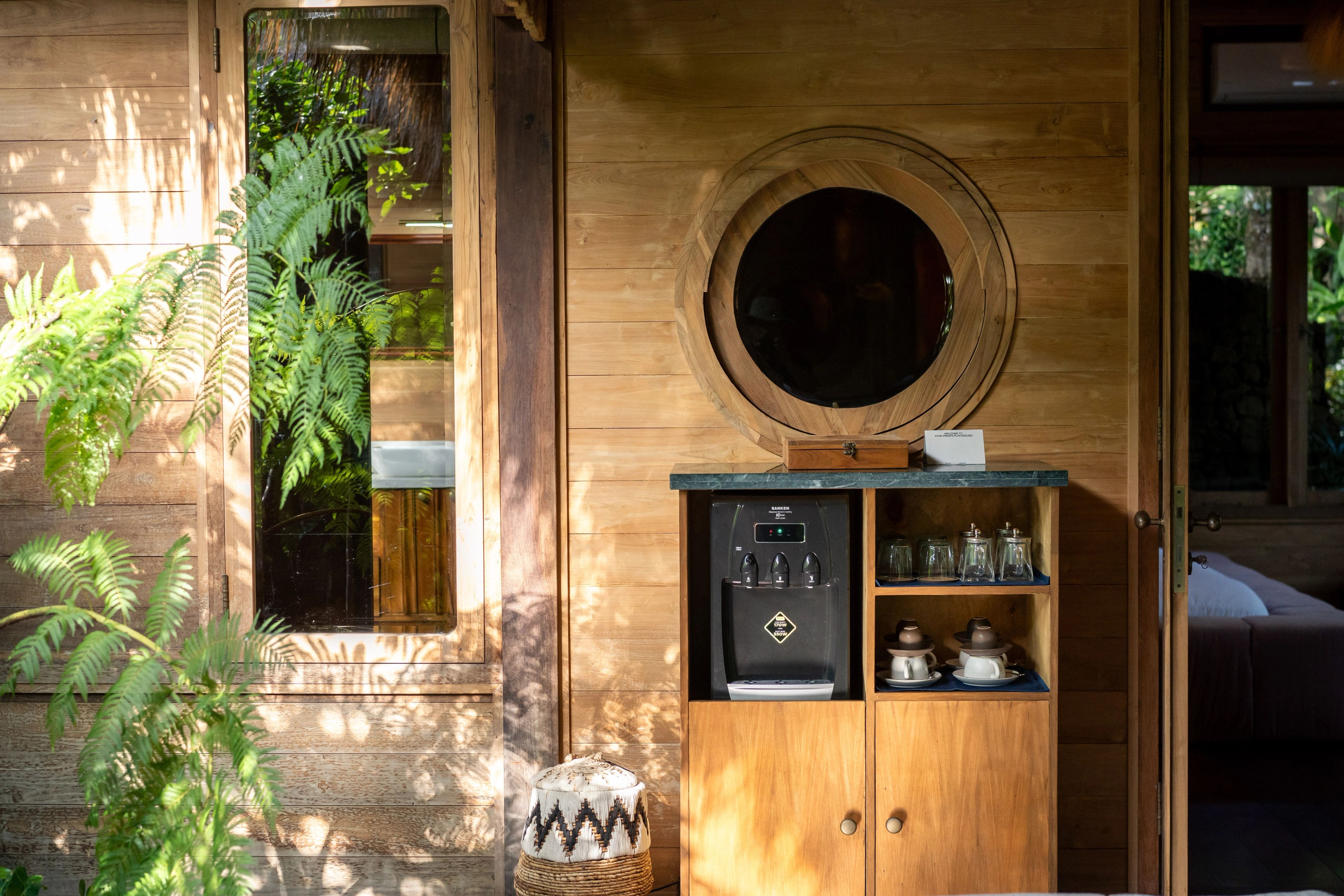 A timber cabinet with a coffee machine, glasses and a round porthole window above it.