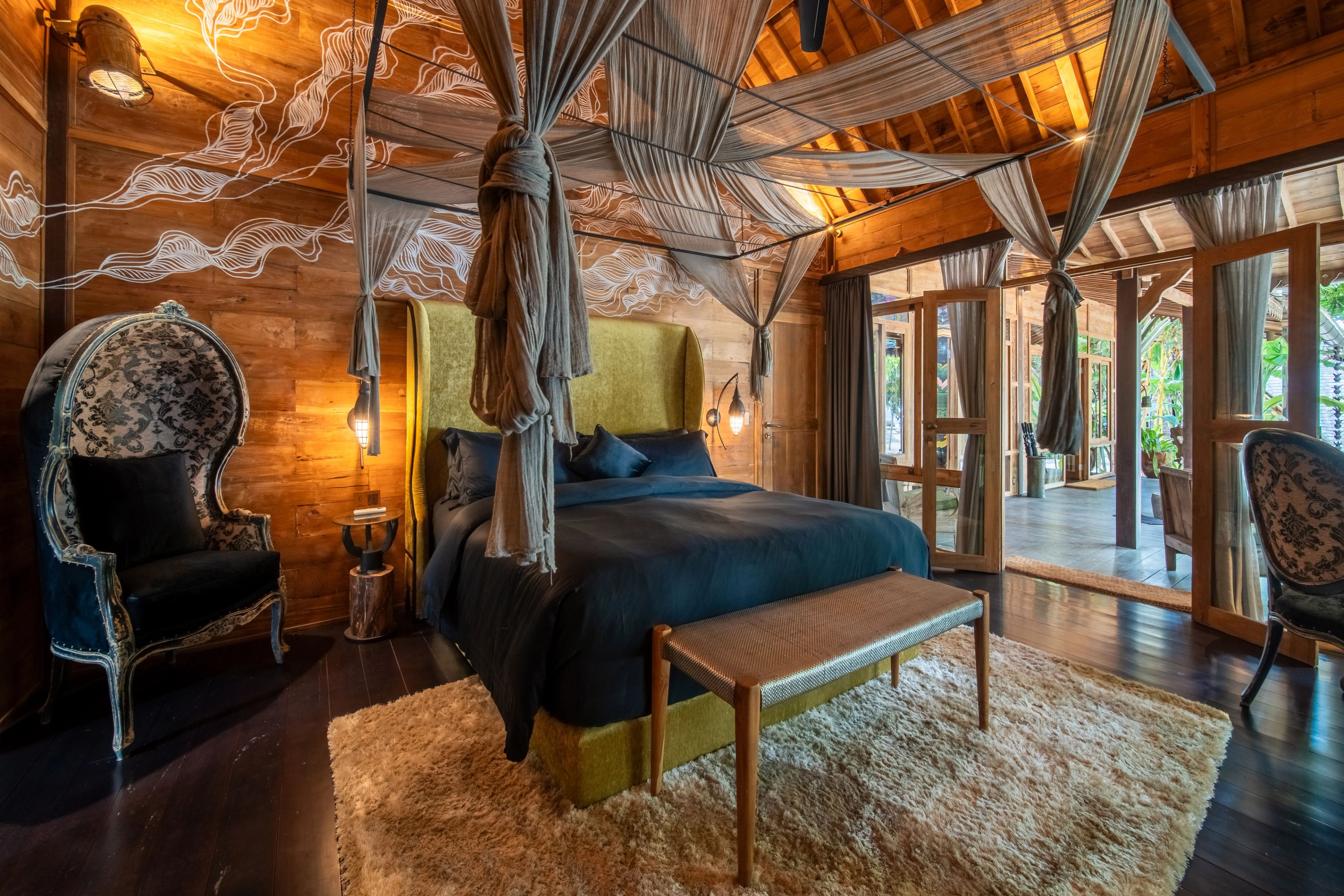 The canopied bed with a patterned armchair beside it, the room opening down the villa's length.