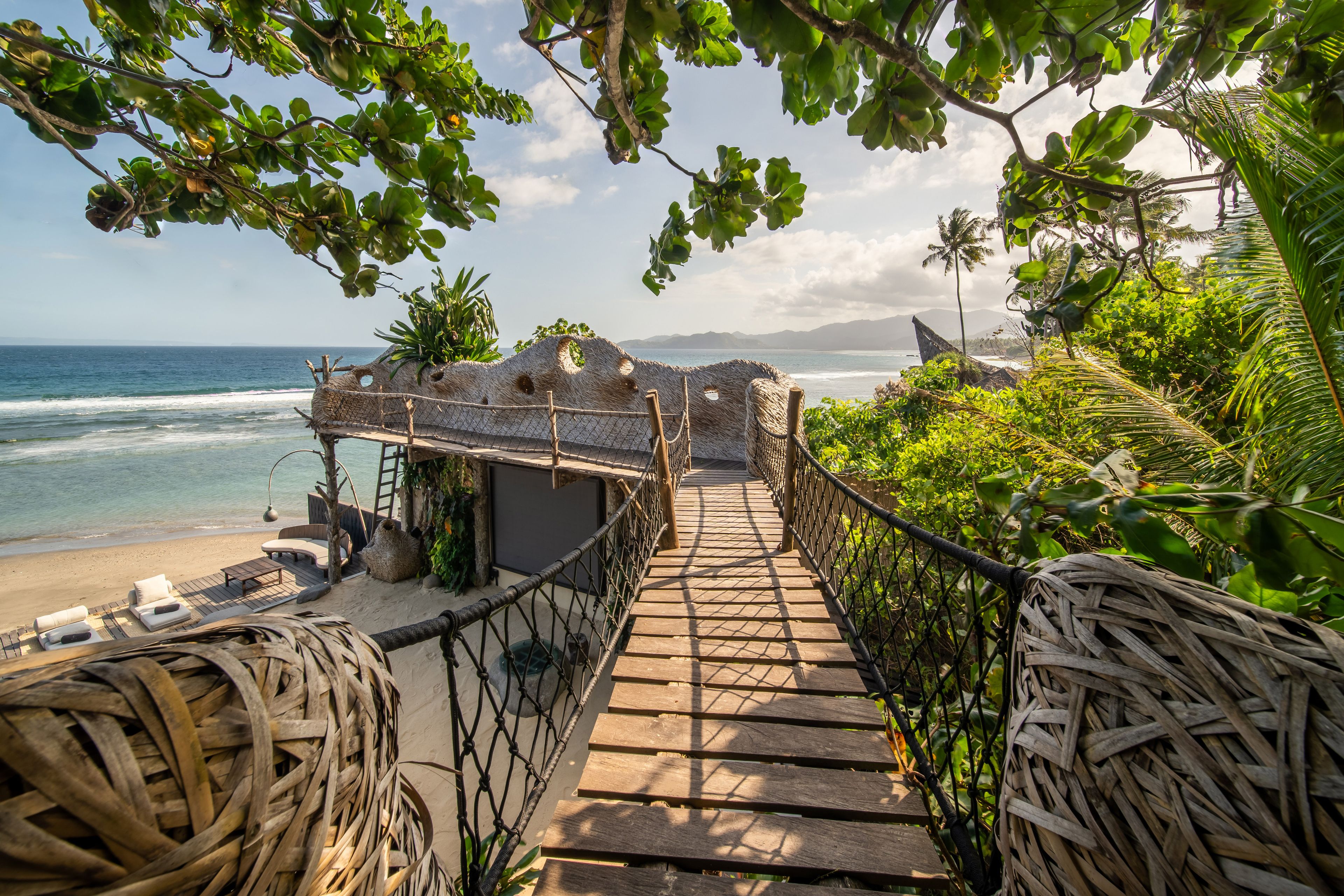 A rope-railed timber bridge running out to the deck above the beach, the sea beyond.