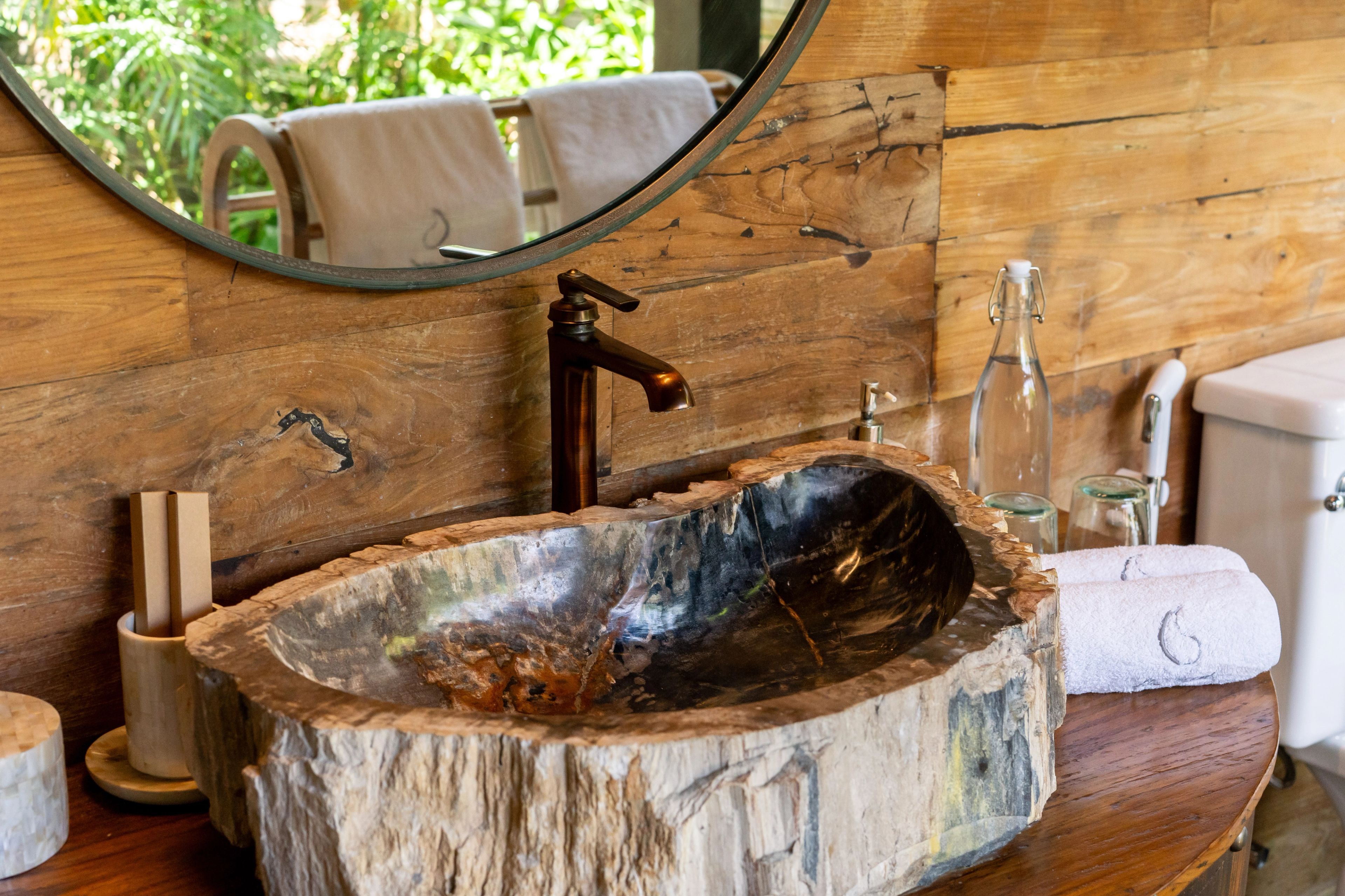 A basin carved from a block of stone on the timber vanity, round mirror above.