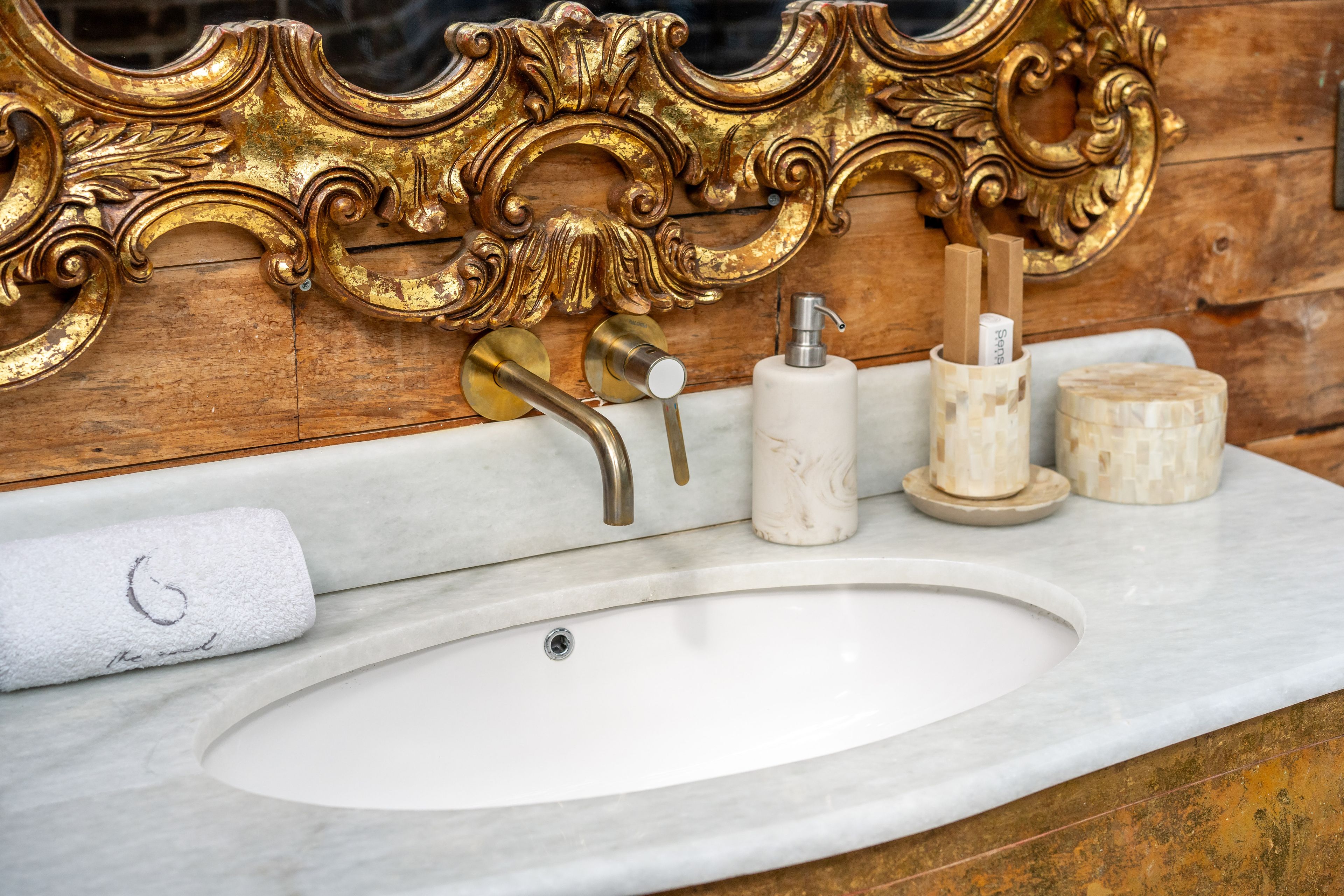 A marble basin below an ornately gilded mirror frame, amenities set on the counter.