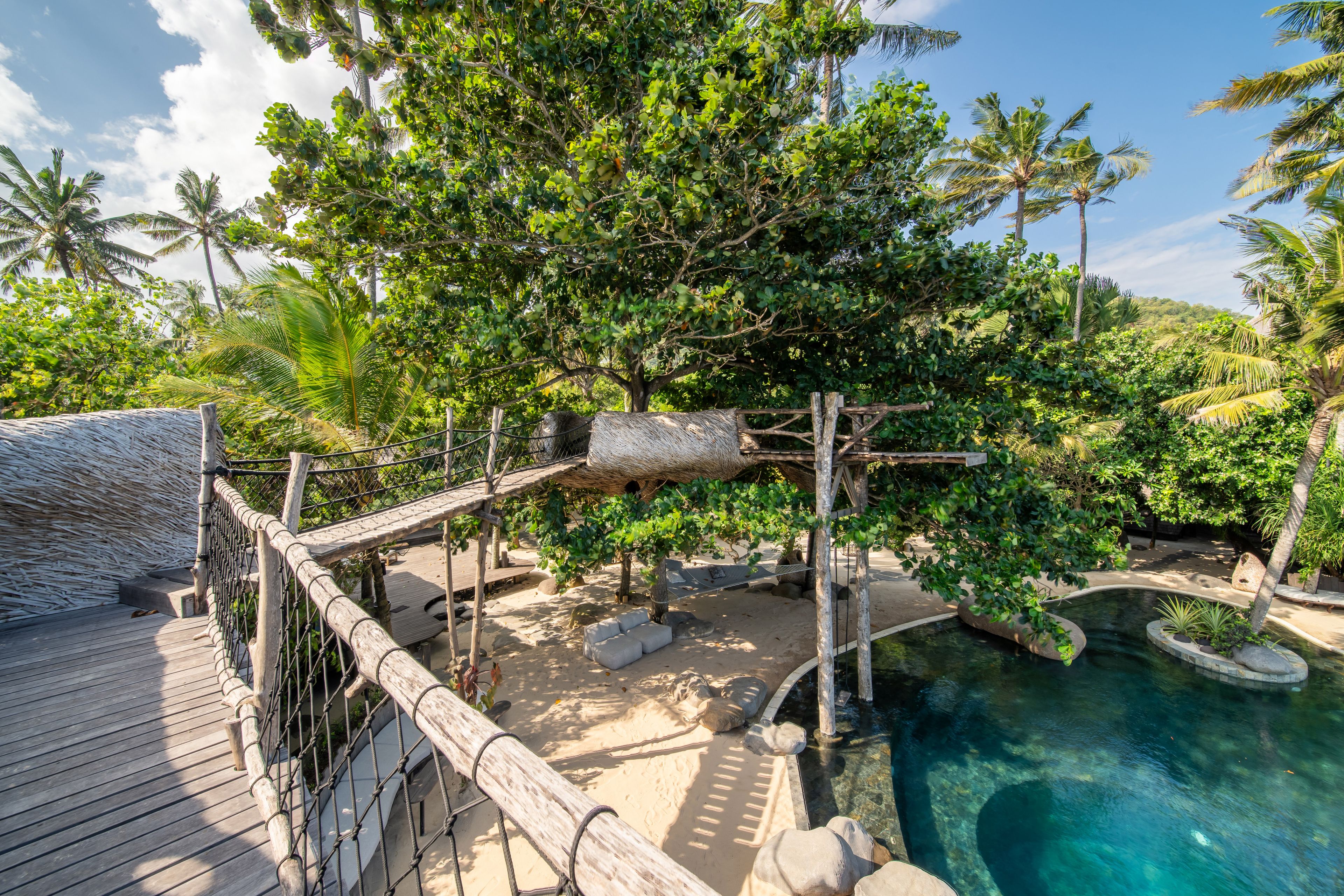 A rope-railed timber bridge crossing above the pool between the trees.