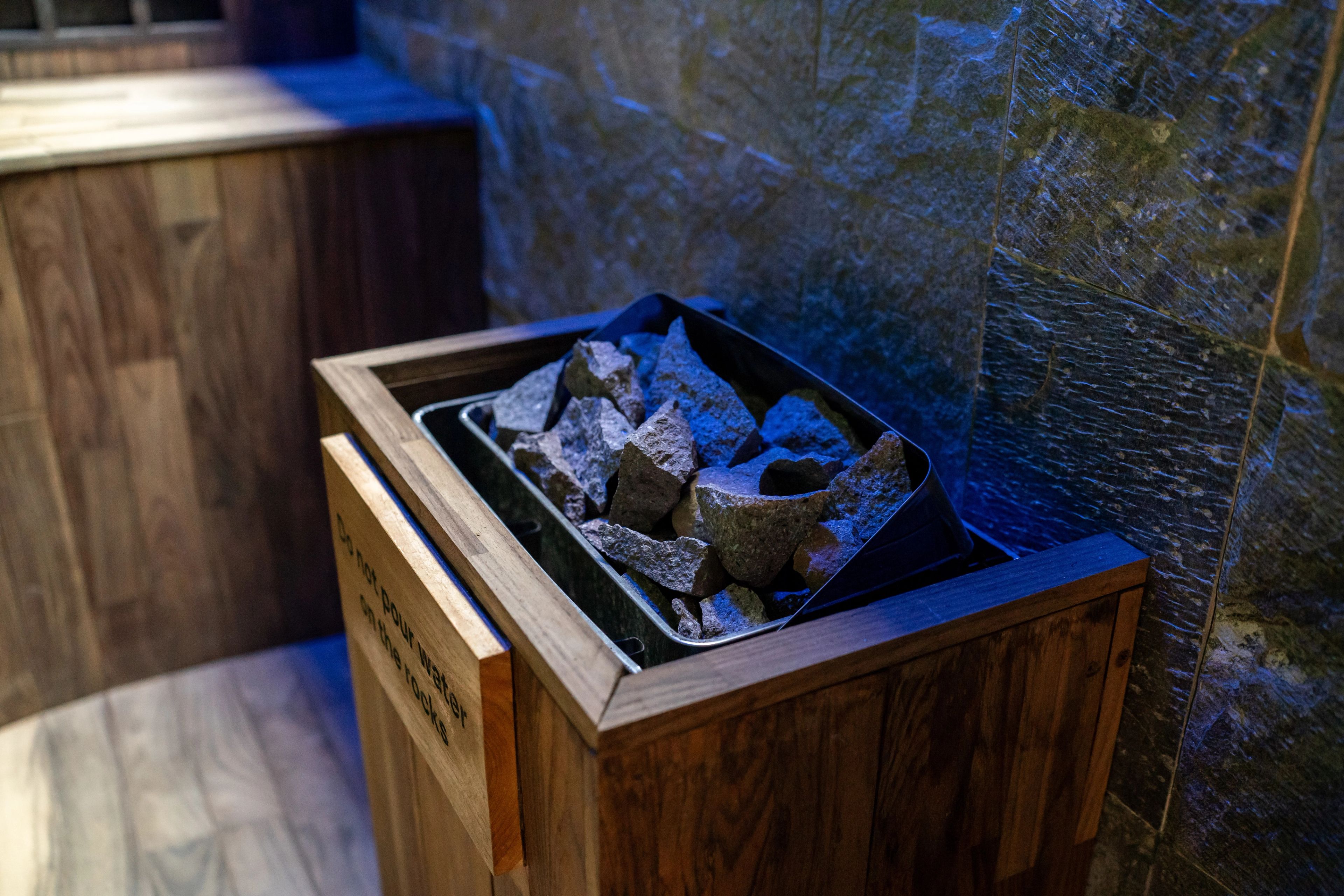 Close-up of the sauna's stone-filled heater set into its timber housing, lit blue.