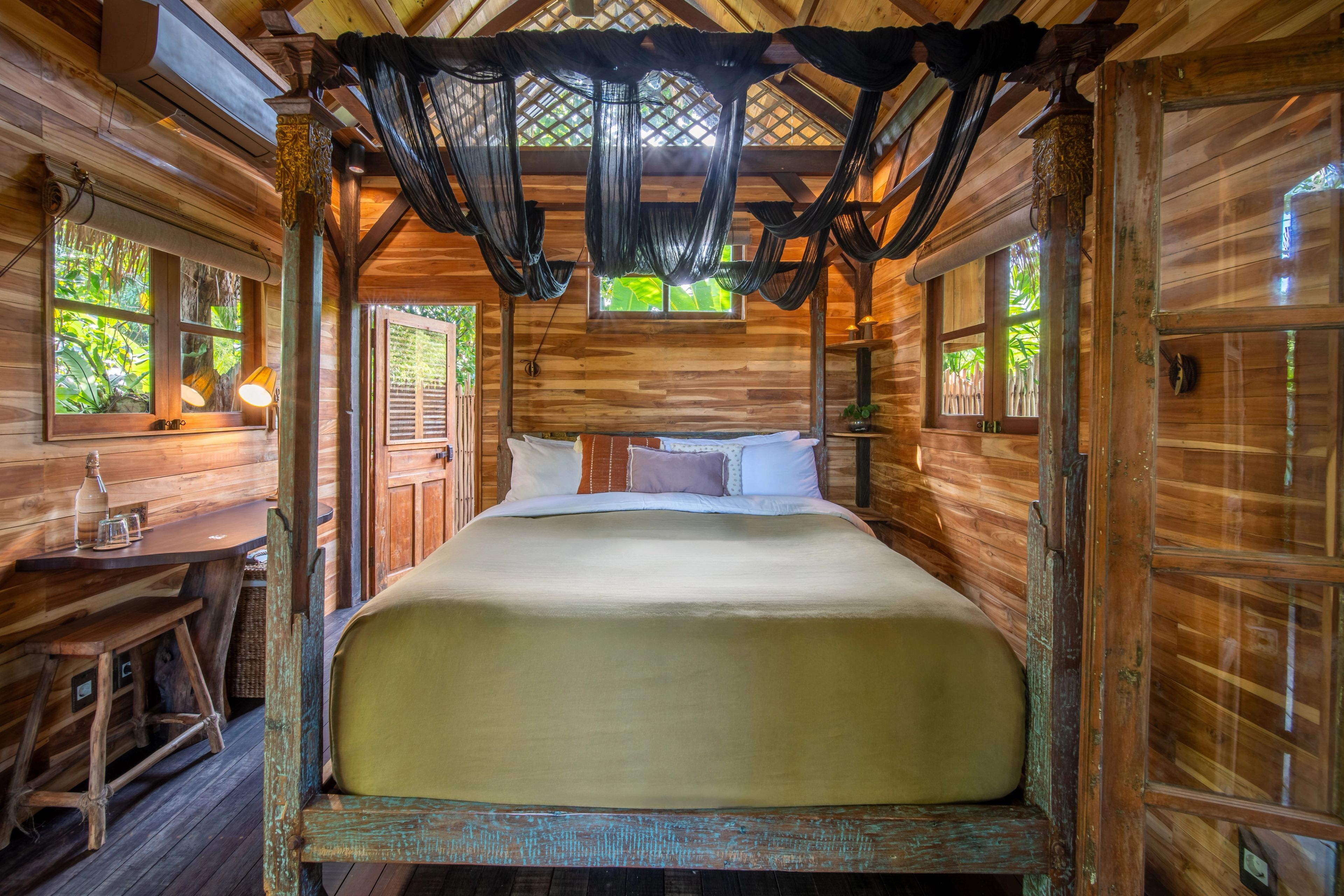 A carved four-poster bed with black netting drawn back, the room open to the deck on two sides.