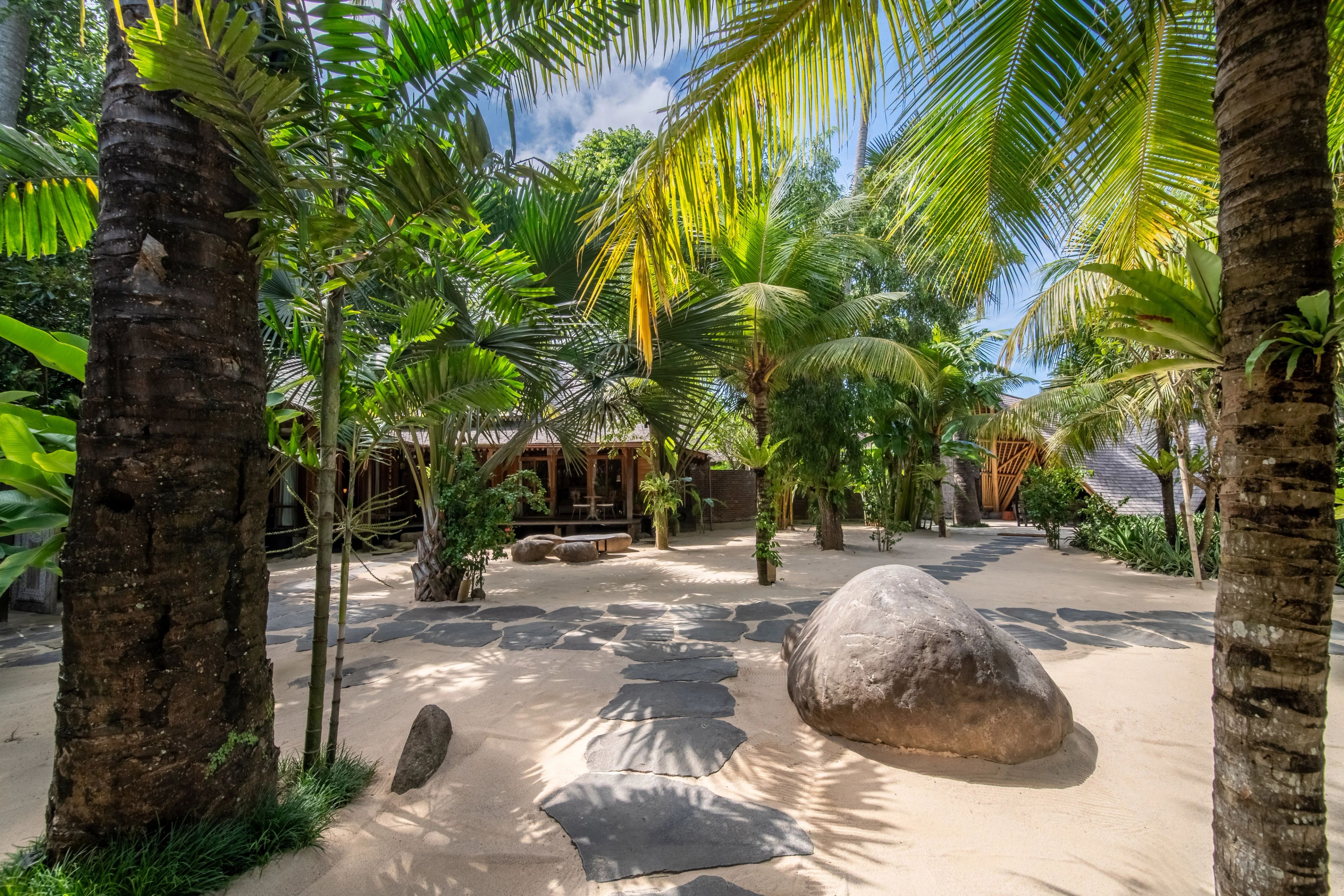 Large boulders set into the raked sand between palms, the villas visible behind.