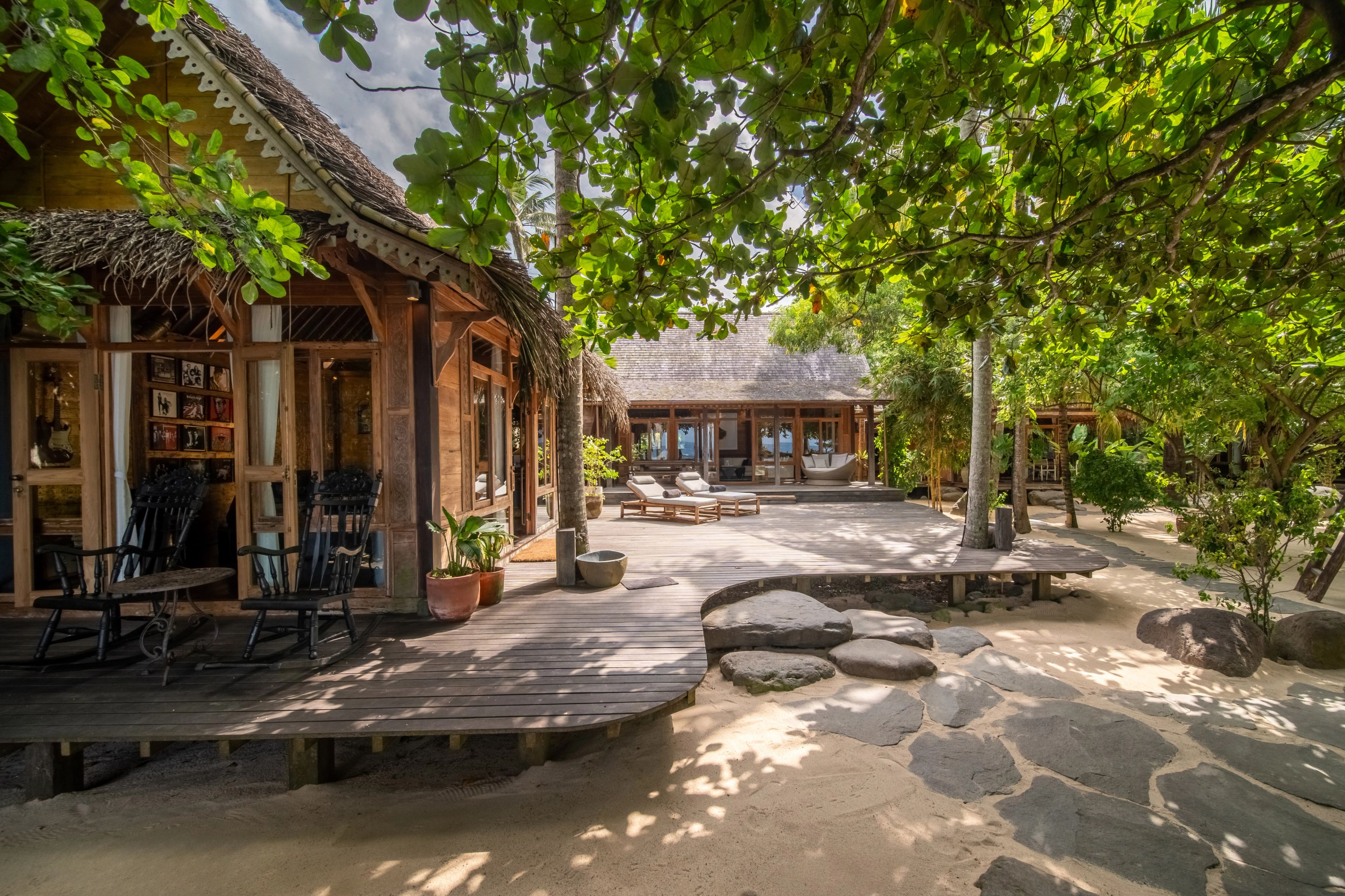 The villa's veranda along one side of the sand courtyard, shaded by a spreading tree.