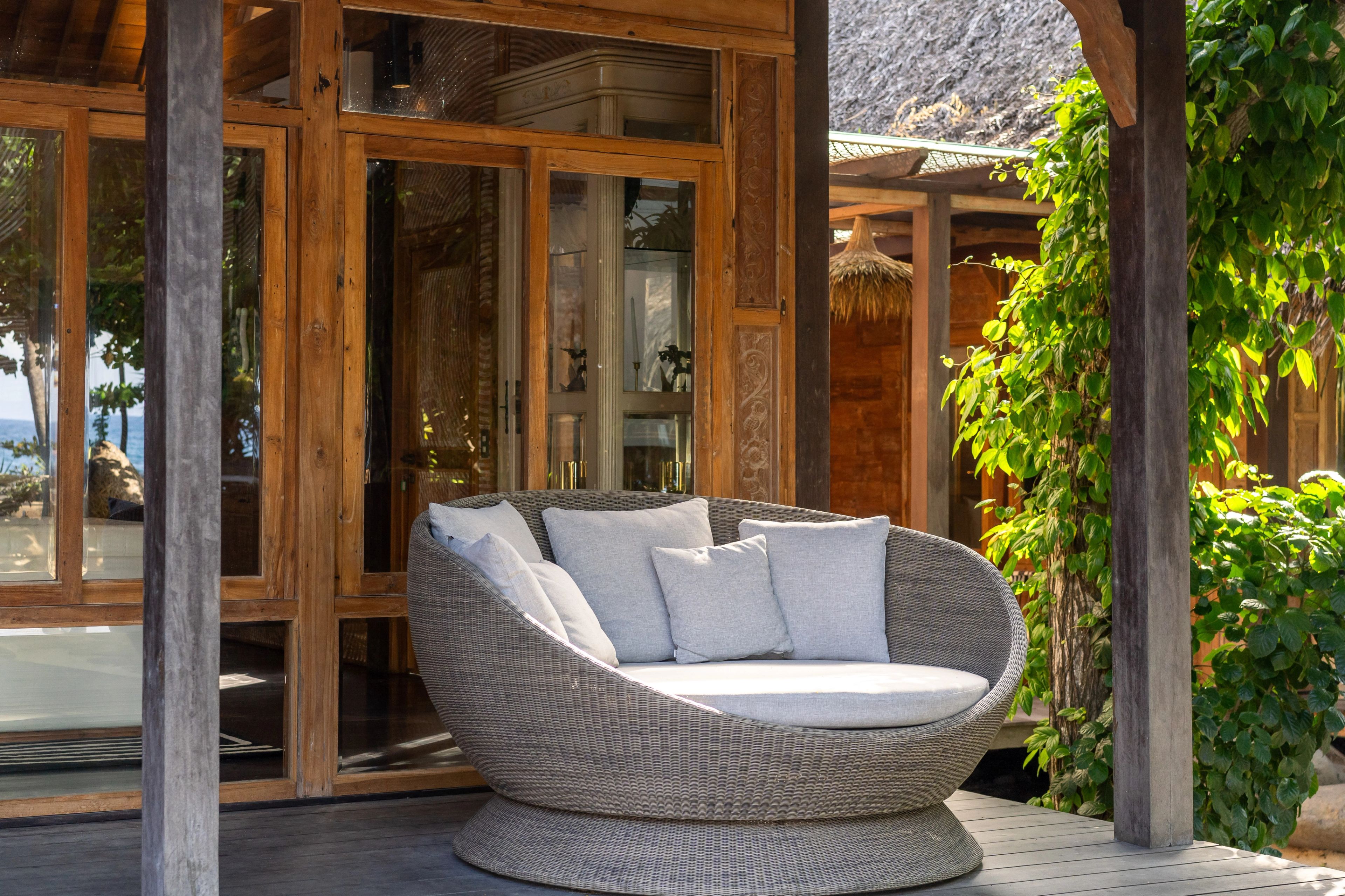 A round woven daybed with cushions on the terrace outside the villa's glass doors.