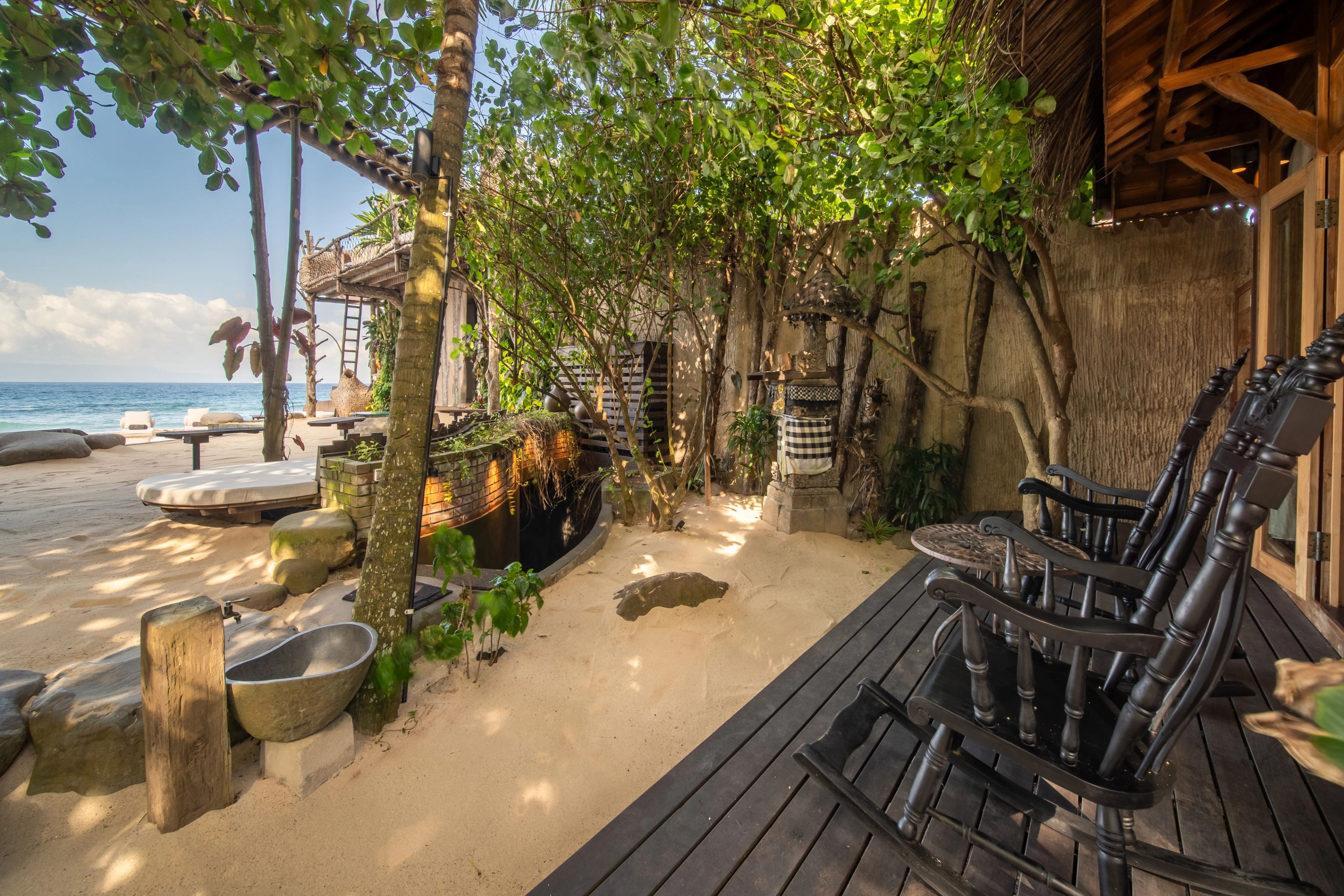 Timber chairs along the villa's deck, looking out past the planting to the sand and sea.