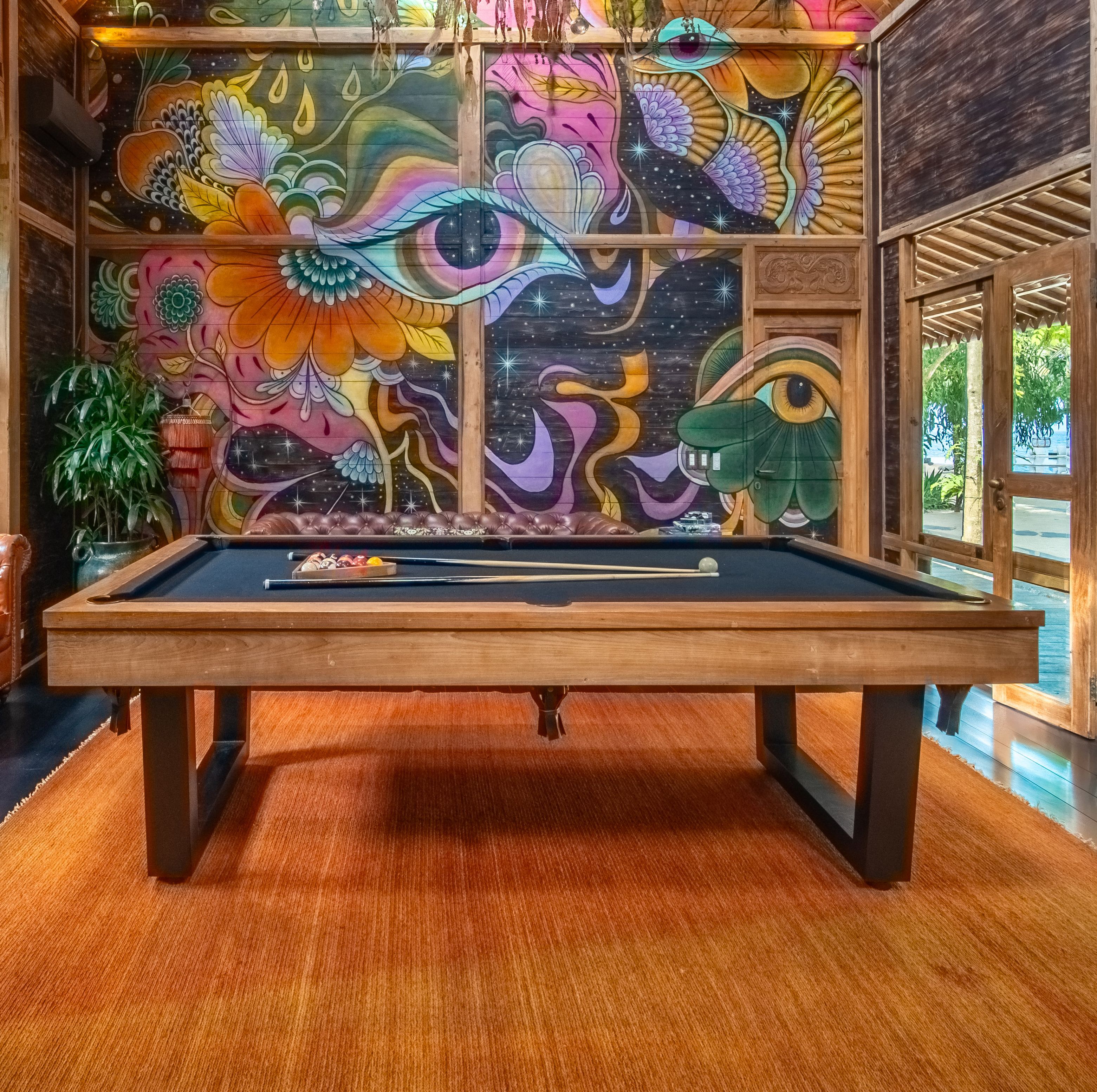 Close-up of a pool table in a wood-paneled games room with jungle views through the window.
