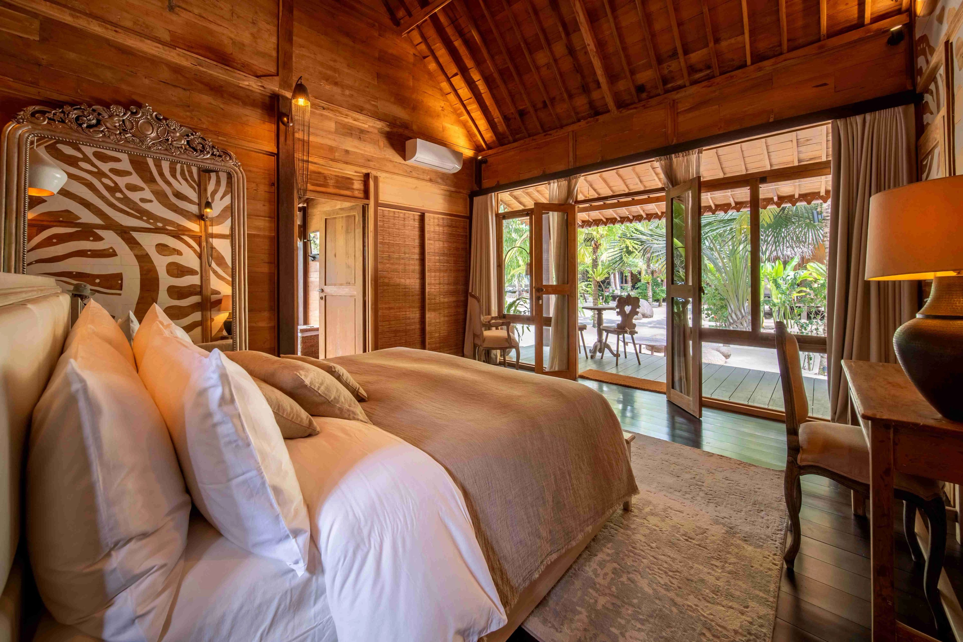 Pillows piled on a made bed, the room opening through glass doors onto the terrace and pool.