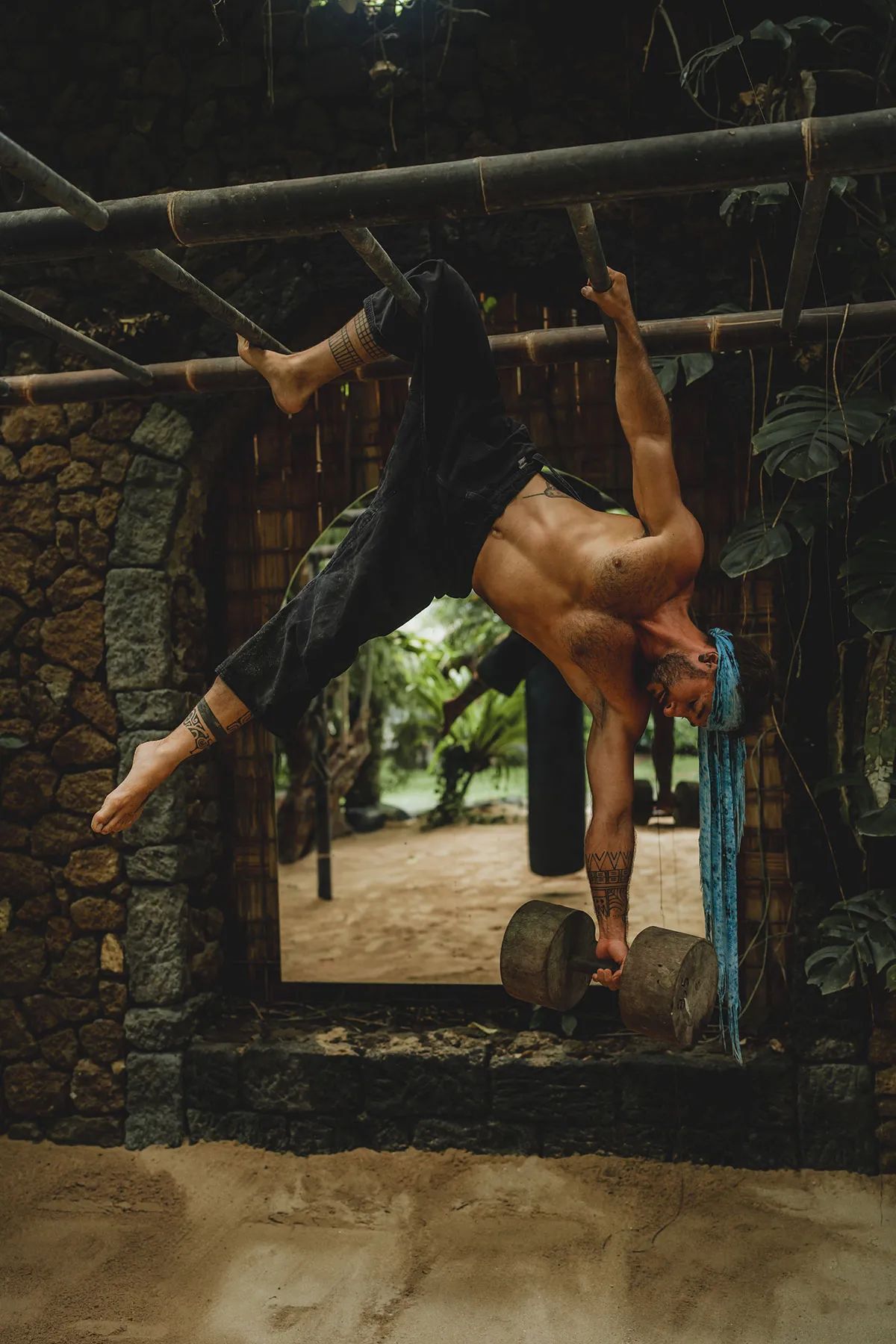 An aerial performer inverted on a hanging silk beside the stone wall of the gym.