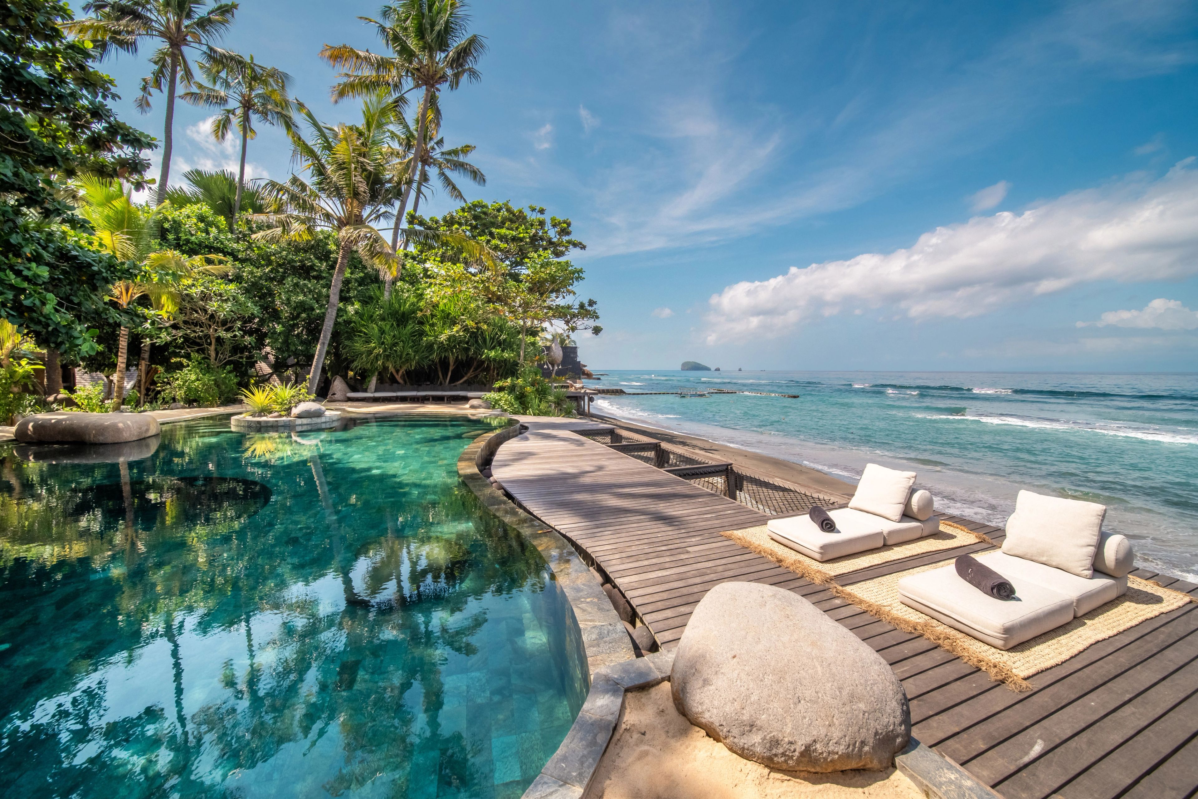 White daybeds along the boardwalk between the pool and the boulders, palms behind.