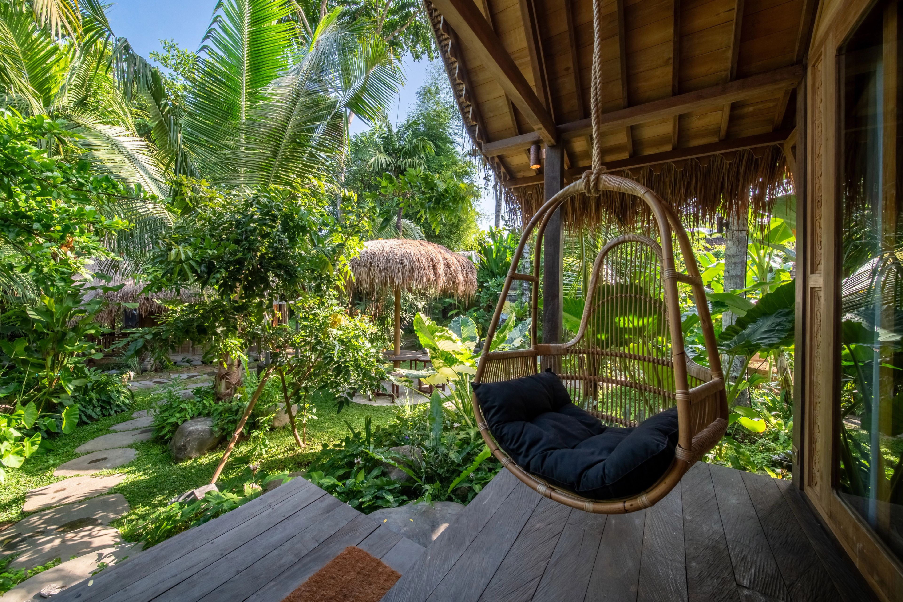 A woven hanging chair on the villa's deck, looking out into the garden and the thatched pavilion beyond.