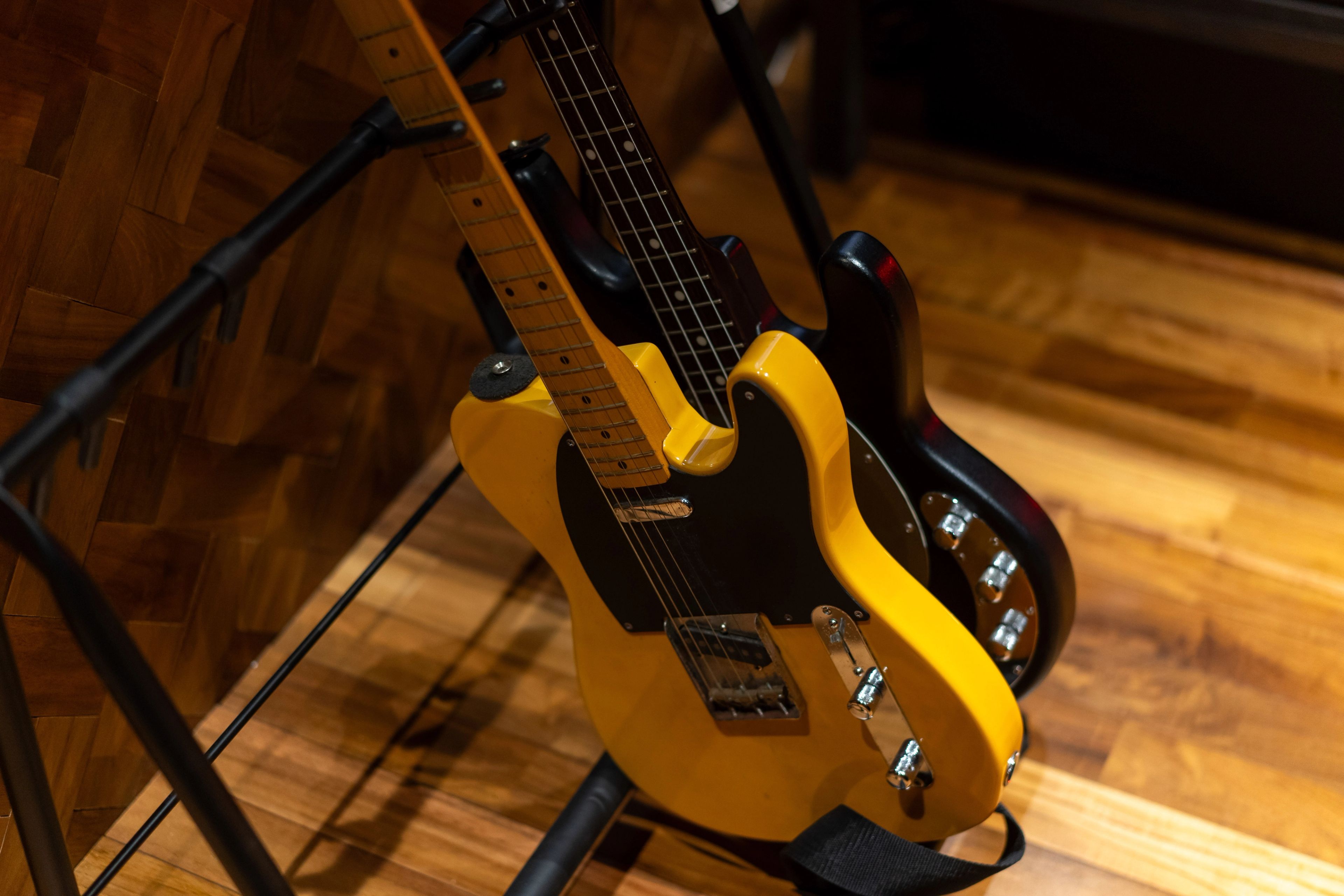 A yellow bass and telecaster resting on stands over the parquet floor.