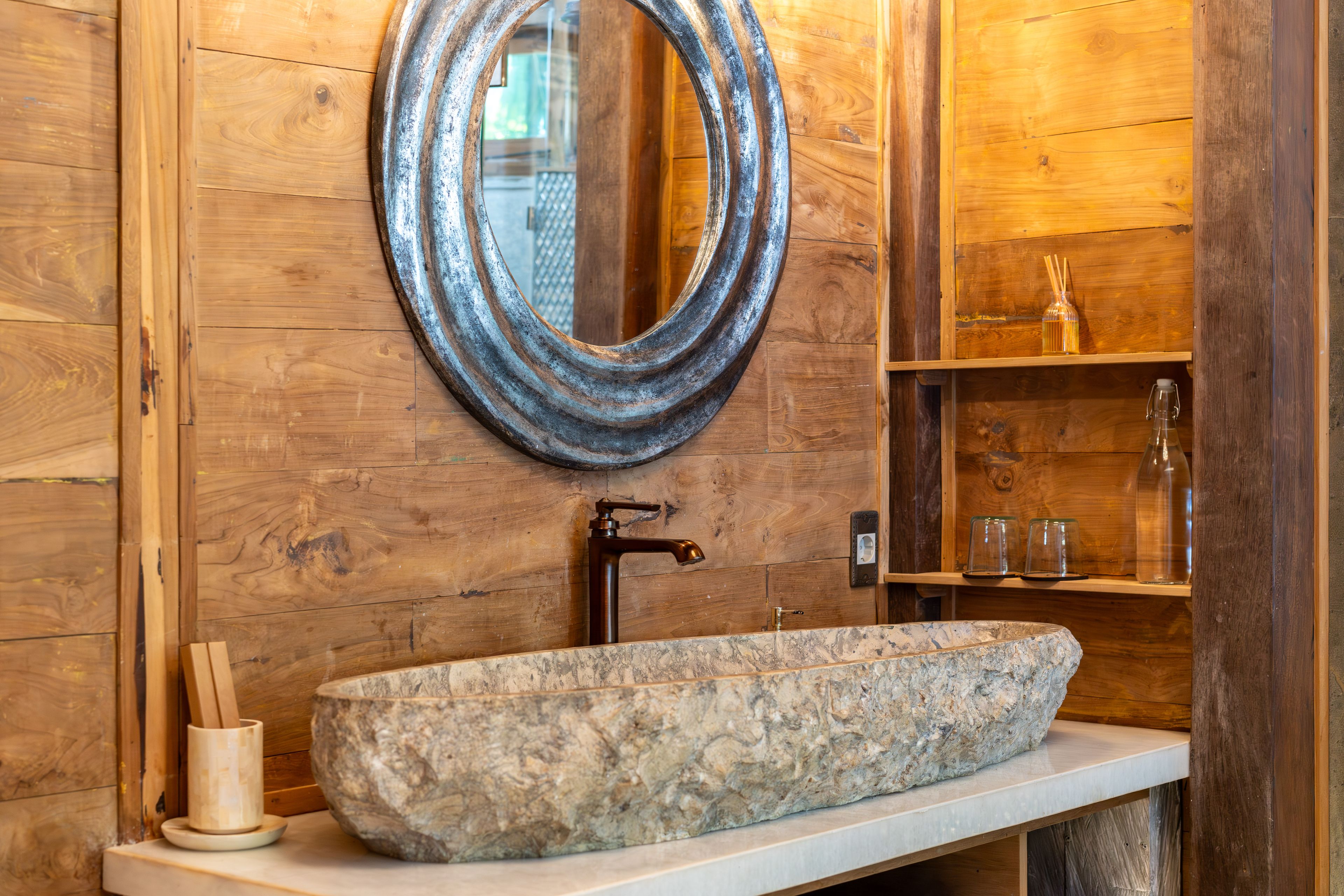 A carved stone basin on a timber shelf below a hammered metal mirror.