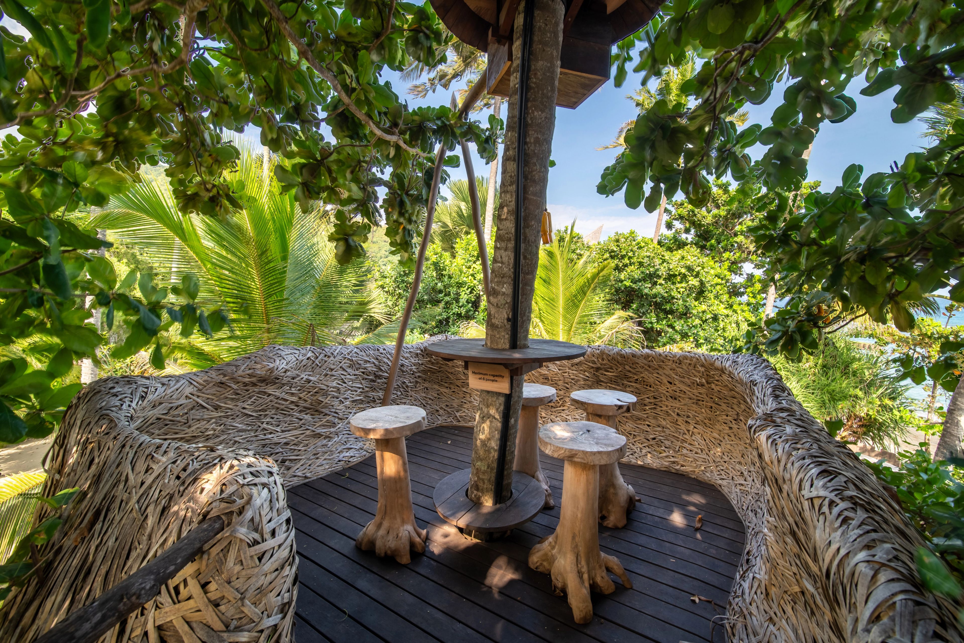 Carved stools around a table on the deck inside the woven nest, open to the trees.