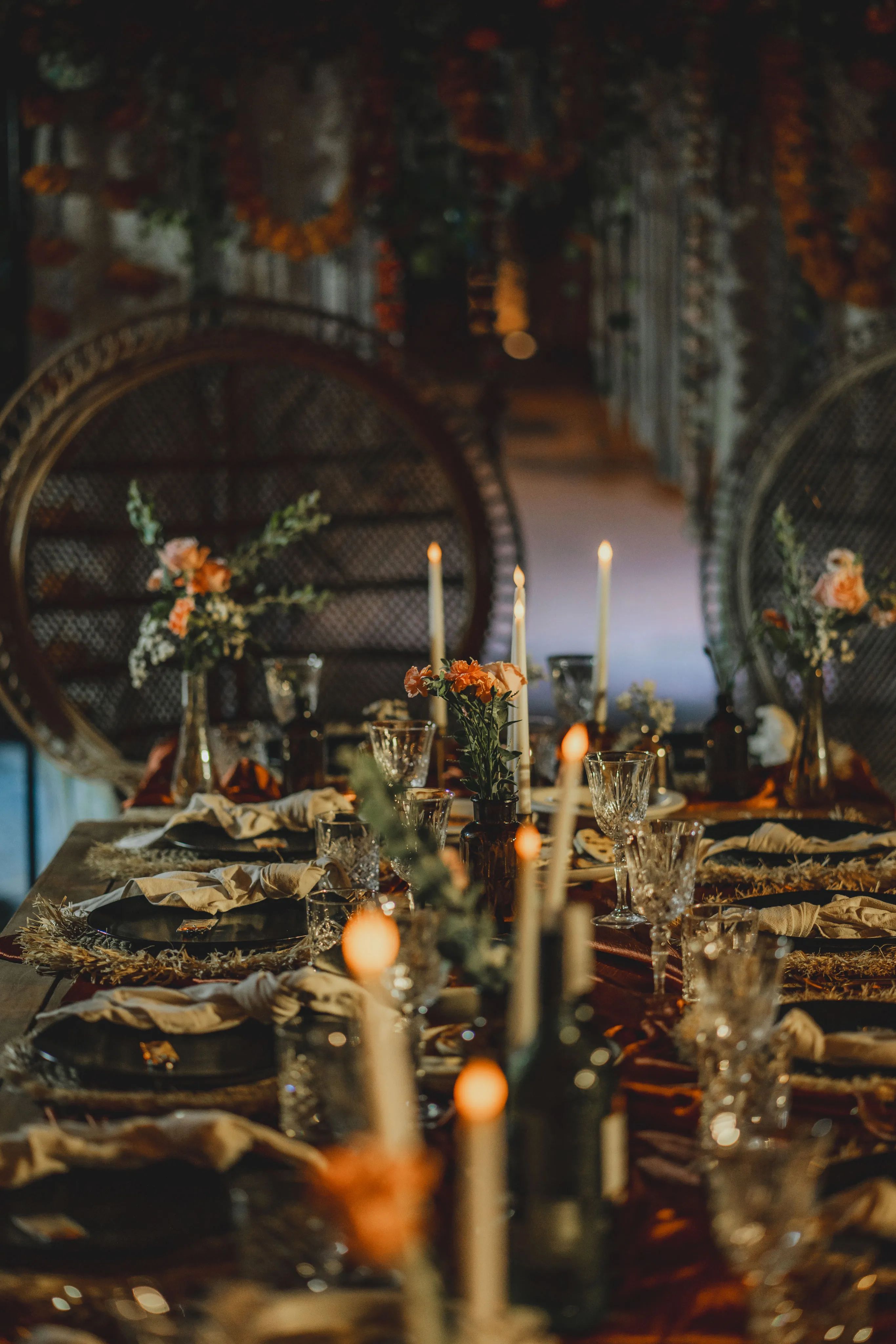A table set with tapers, glassware and low flower arrangements, laid inside a woven pod at night.