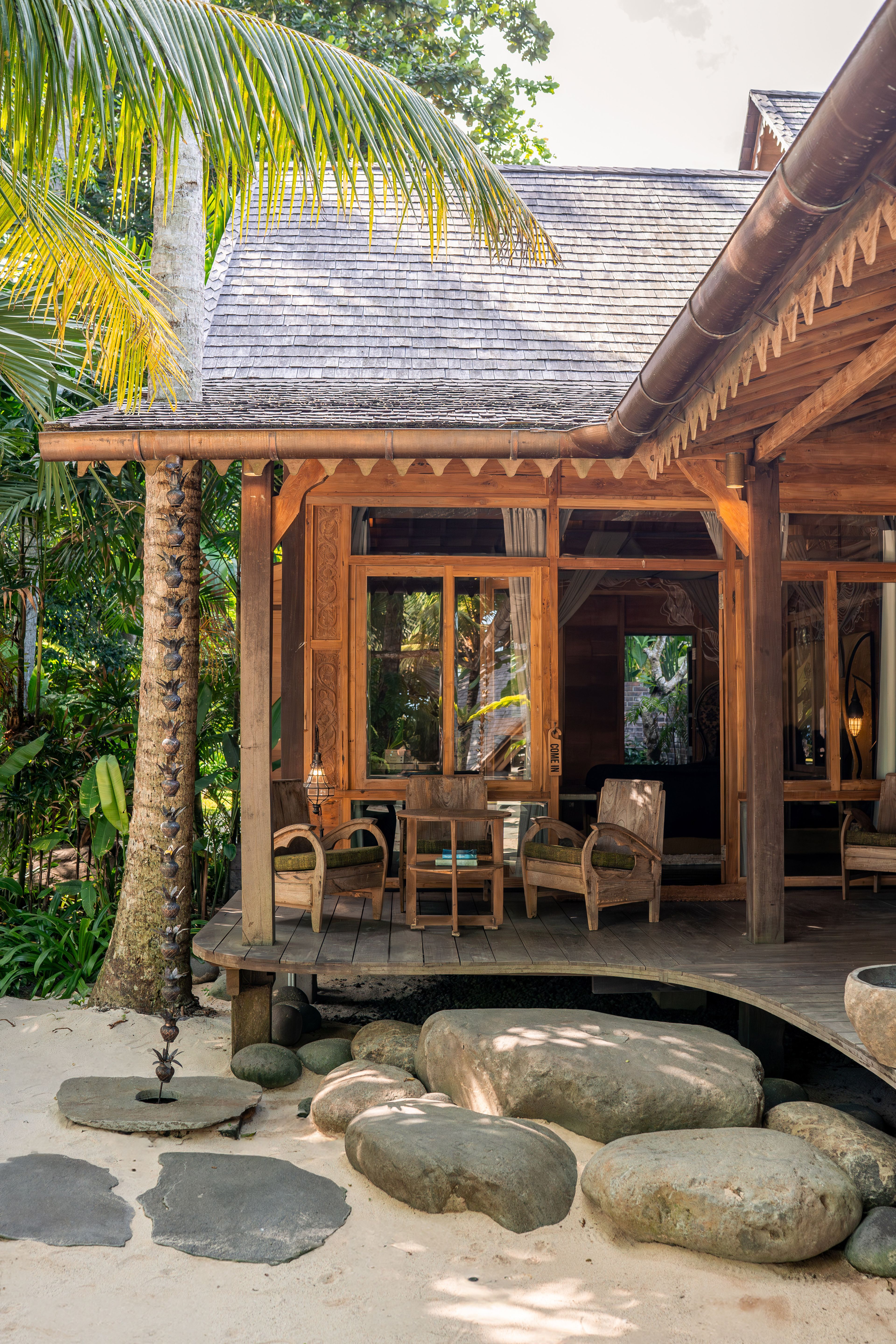 Cane armchairs and a table on the villa's veranda, seen from the courtyard through the palms.