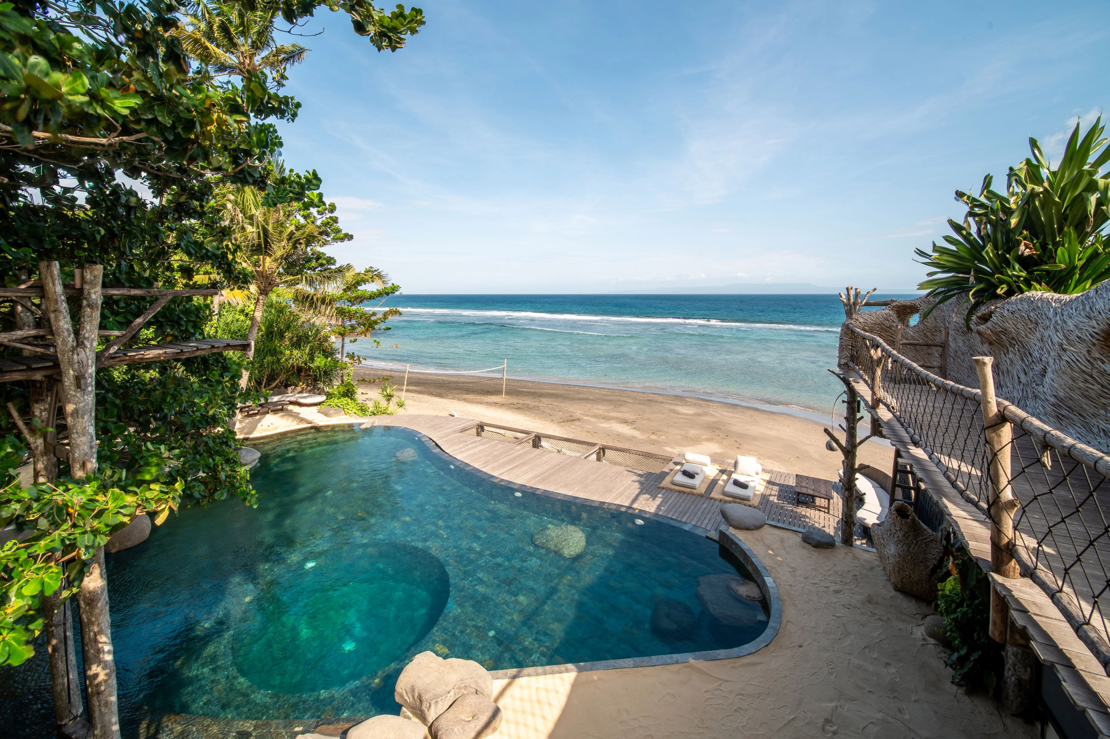 Pool deck overlooking a beach volleyball net and the ocean at The Seed Bali.