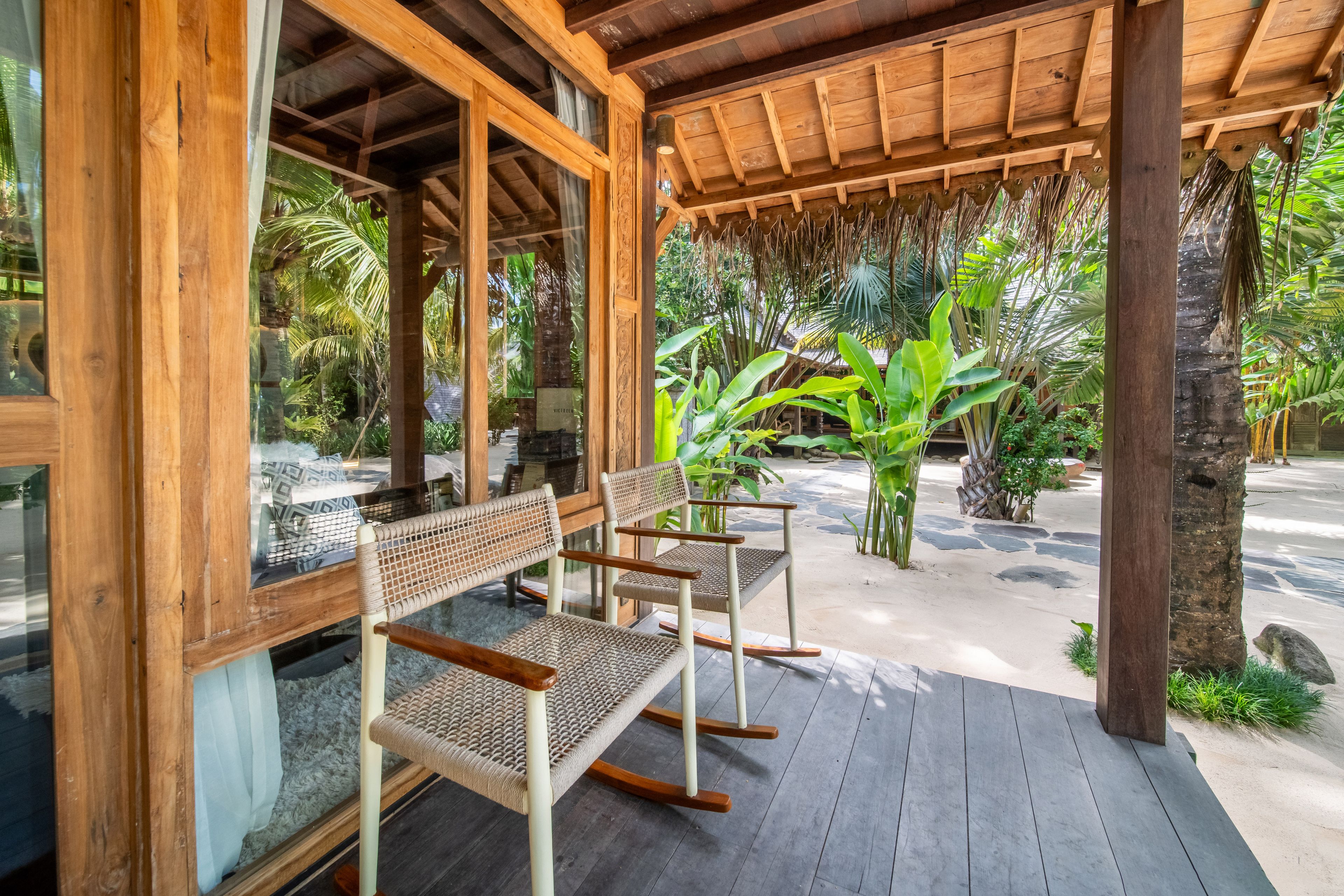 Cane chairs and a low table on the veranda, the courtyard and palms beyond the posts.